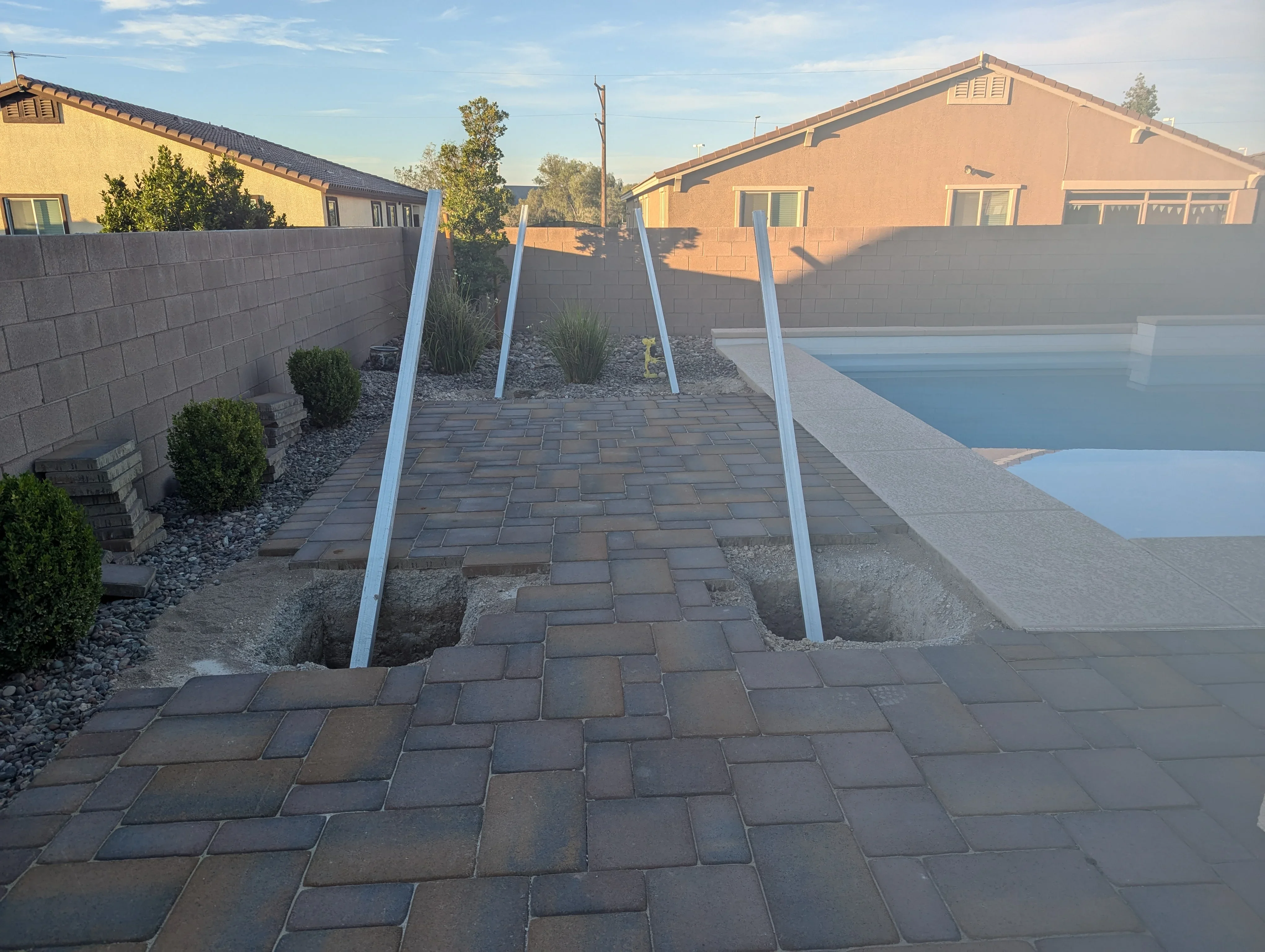 Paver patio with white pergola posts overlooking pool and residential homes