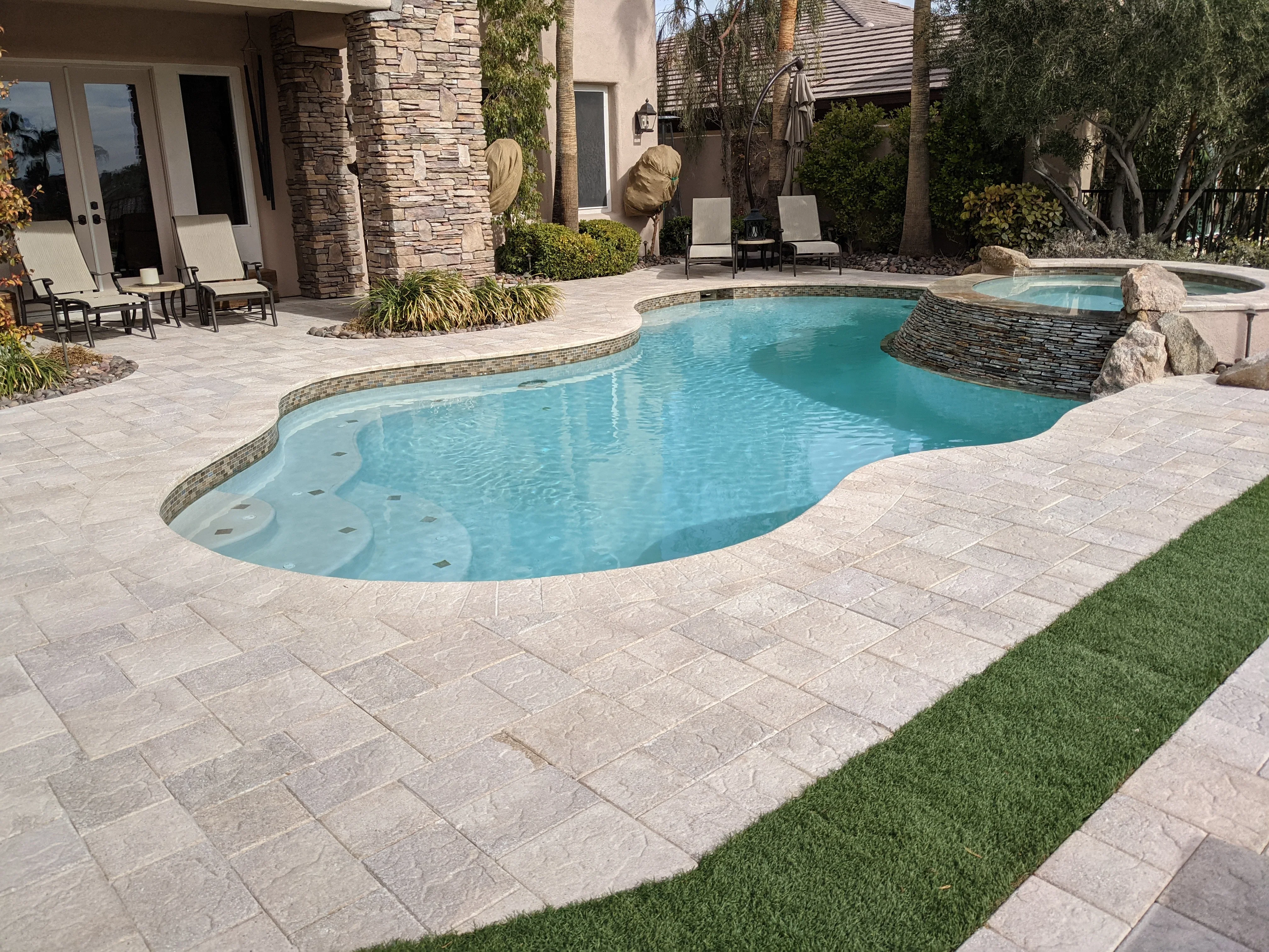 Luxury backyard with turquoise pool, travertine patio, and stone features