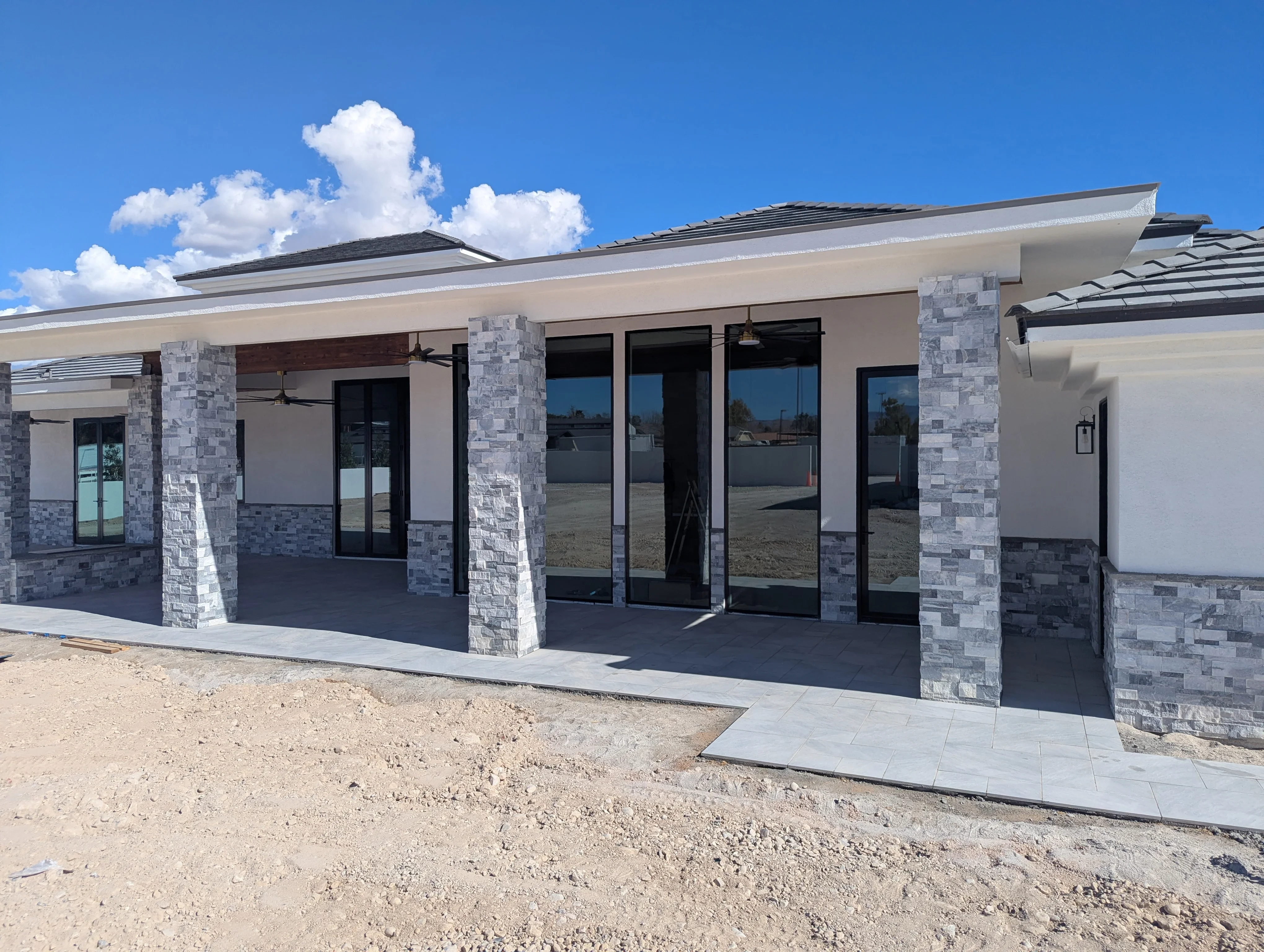 Modern patio with stone pillars, concrete foundation, and black-framed glass doors under clear sky