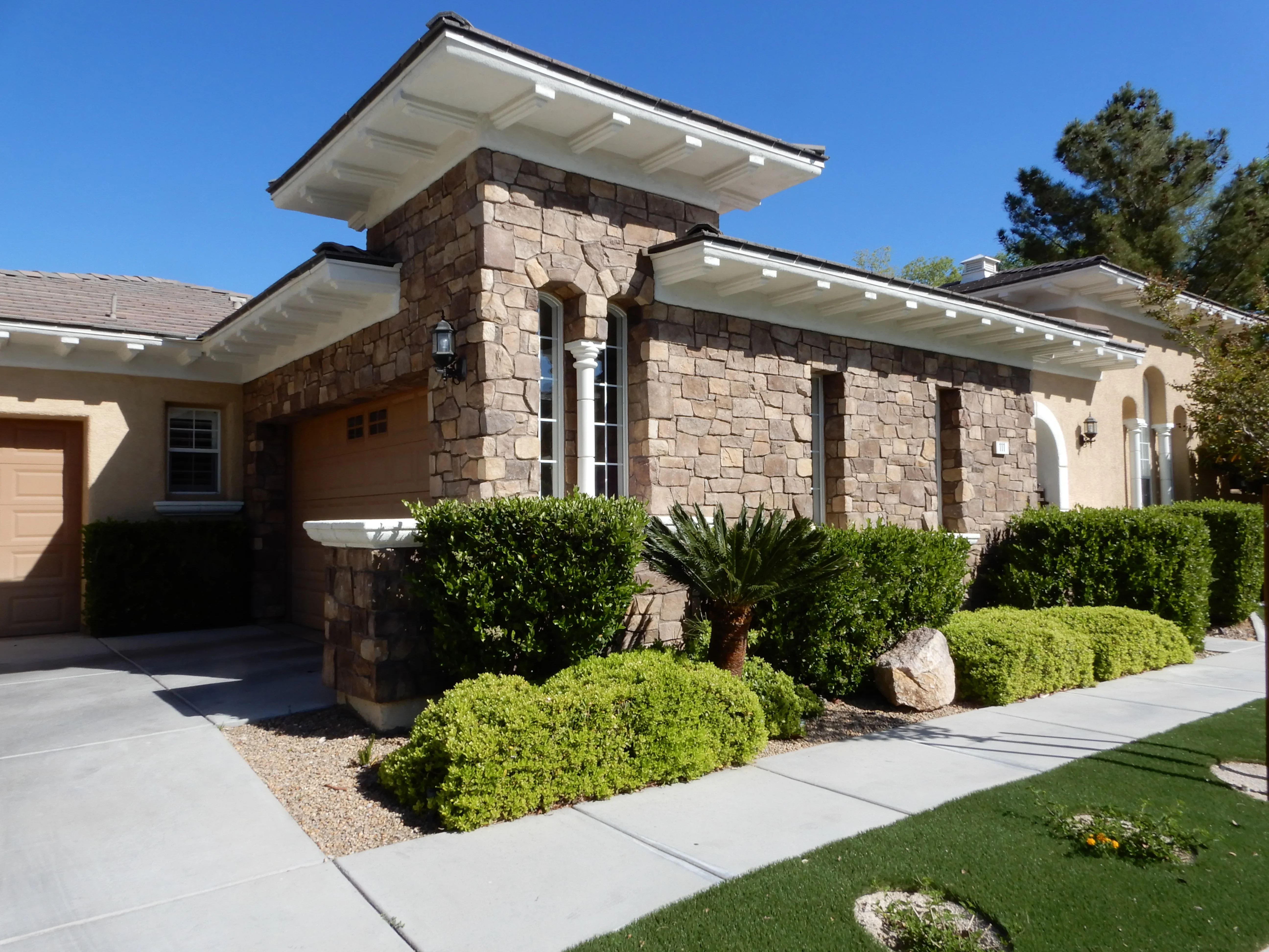 Modern home with stacked stone facade, white soffit overhangs, and concrete hardscape with landscaping