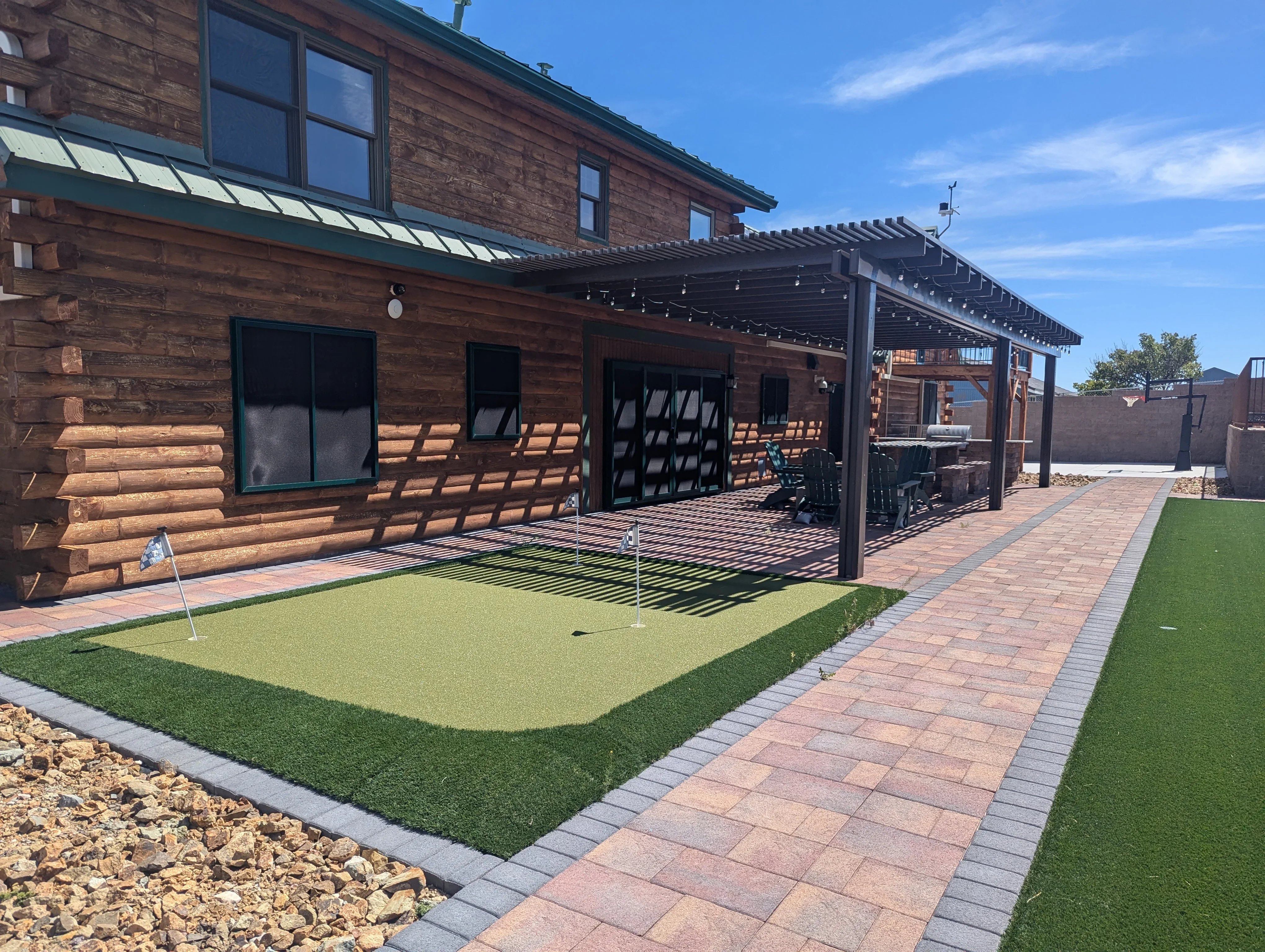 Backyard patio with synthetic putting green, brick pavers, and black metal pergola
