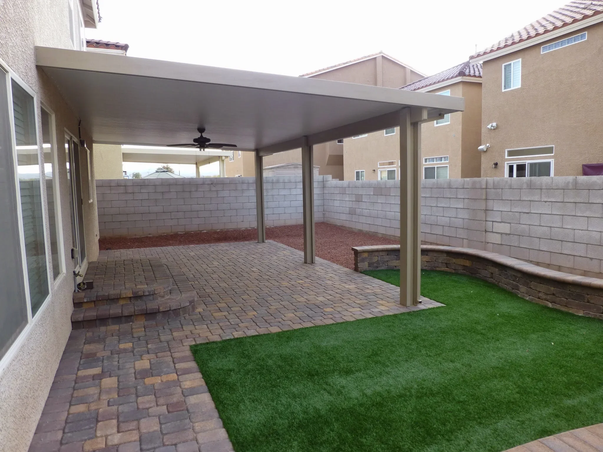 Covered patio with pergola, paver flooring, privacy wall, and synthetic grass in residential backyard