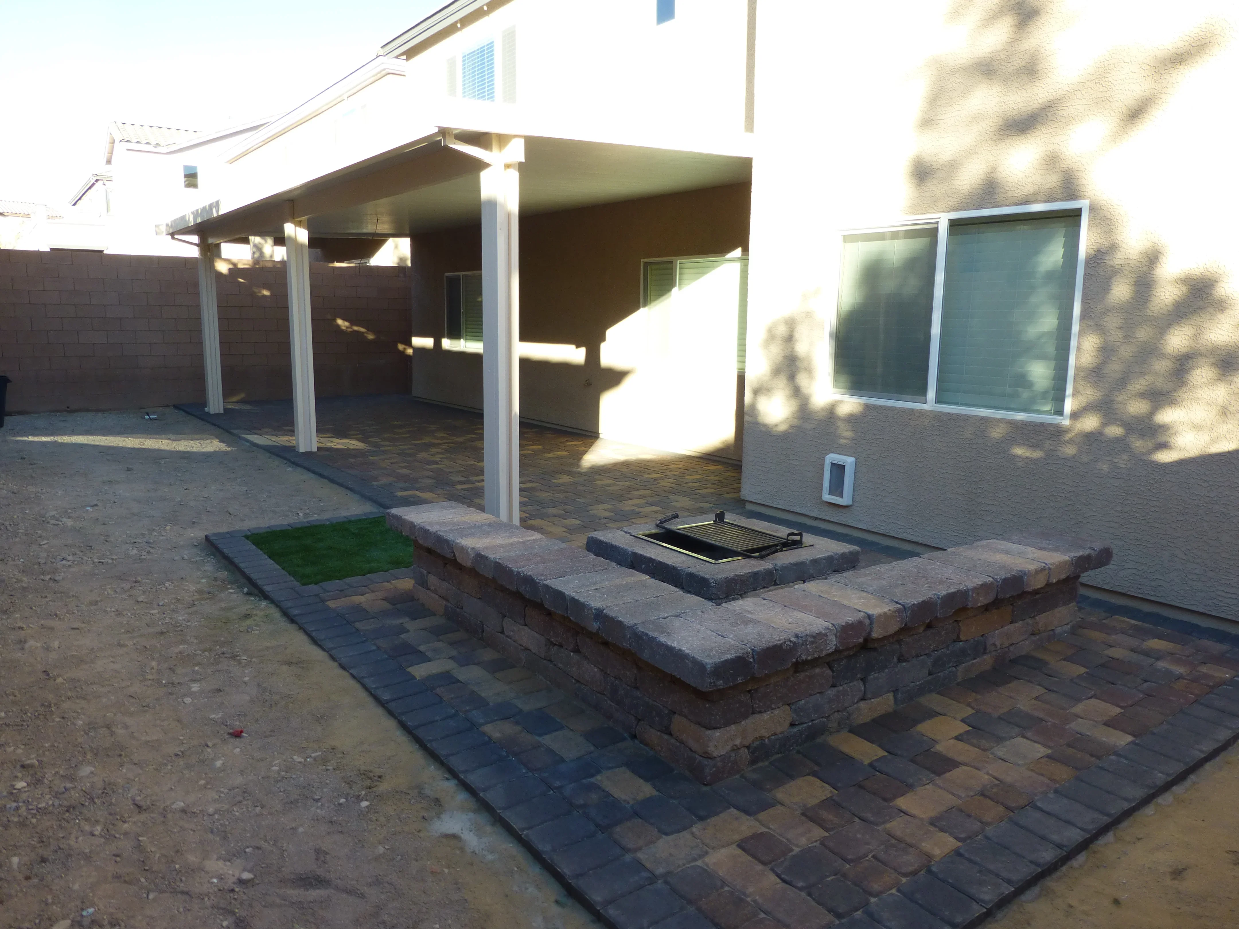 Backyard patio with brick fire pit, paver deck, and white pergola structure