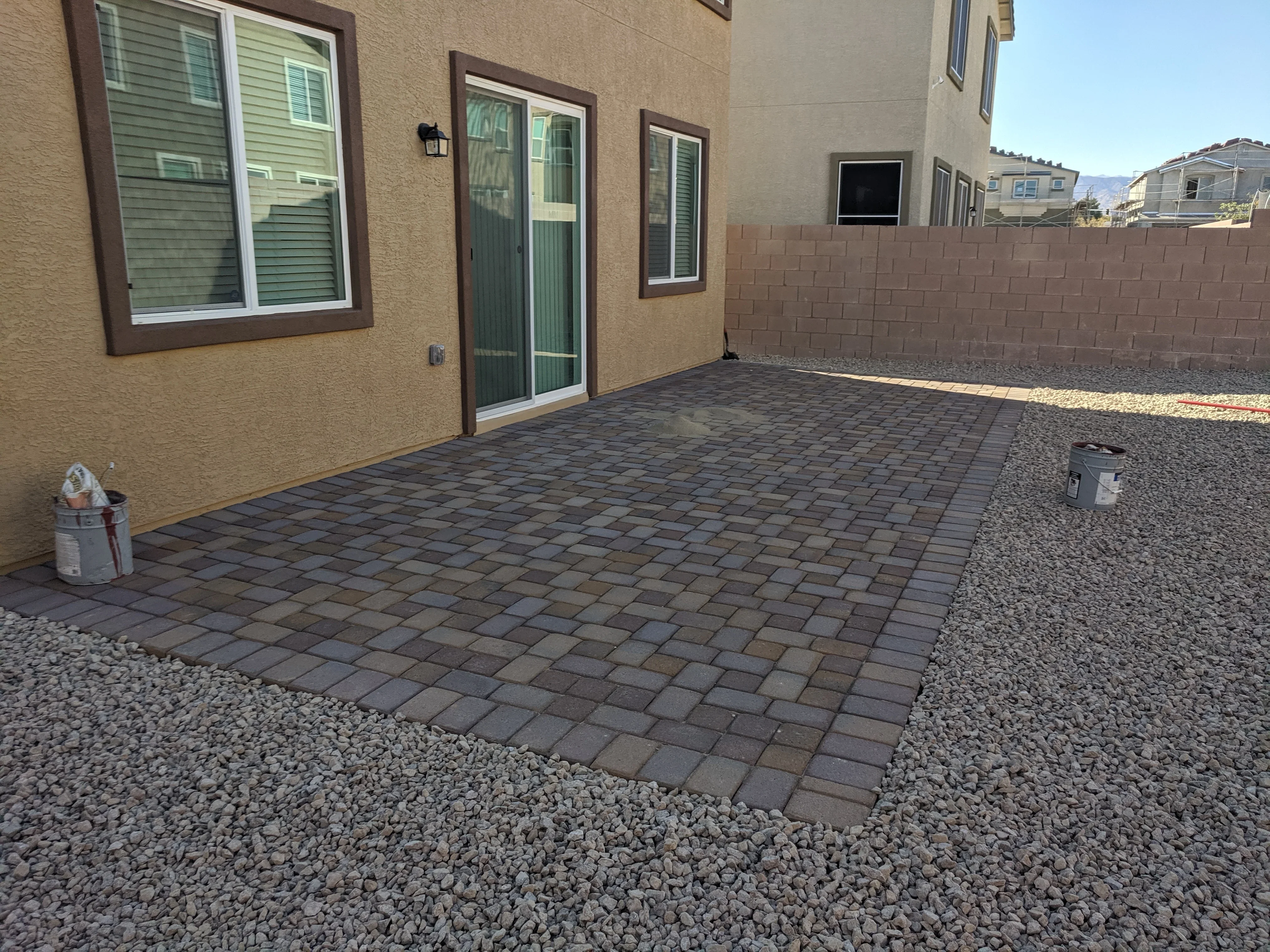 Dark gray permeable pavers form a patio bordered by light gravel against a tan stucco home