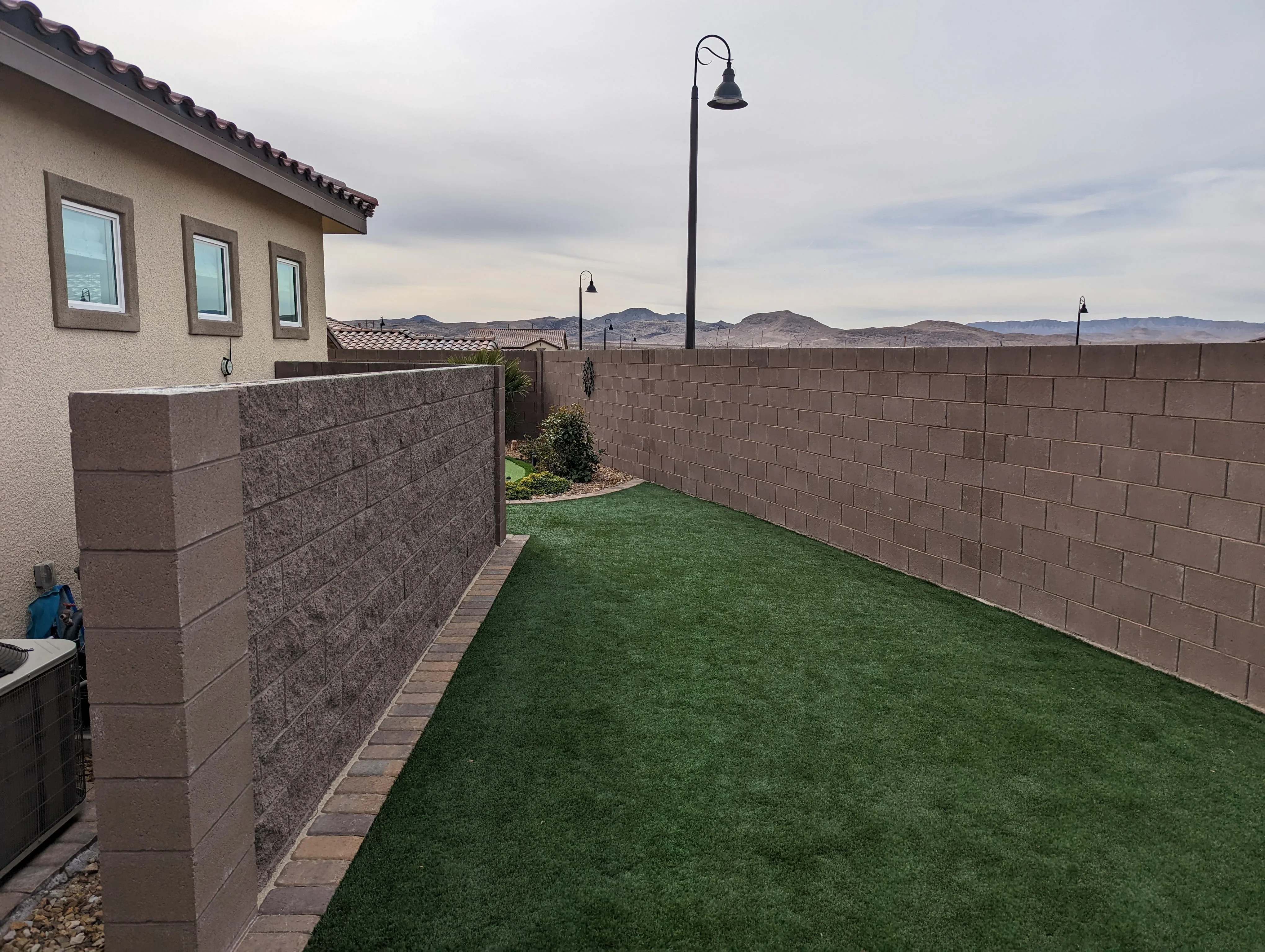 Backyard with brown concrete block retaining wall, synthetic grass, and landscape lighting poles