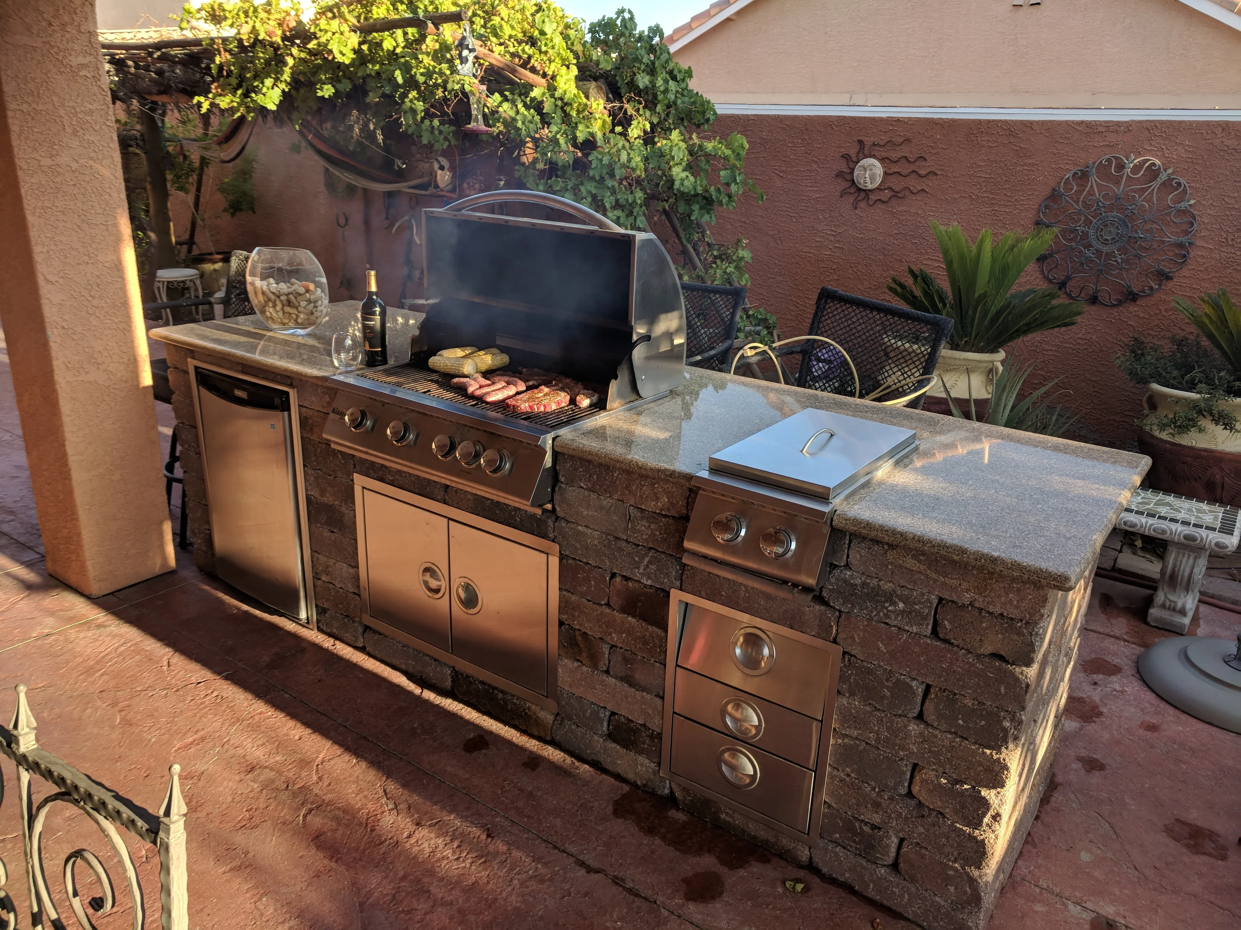 Built-in outdoor kitchen with stone base, stainless steel grill, and pergola in Las Vegas patio