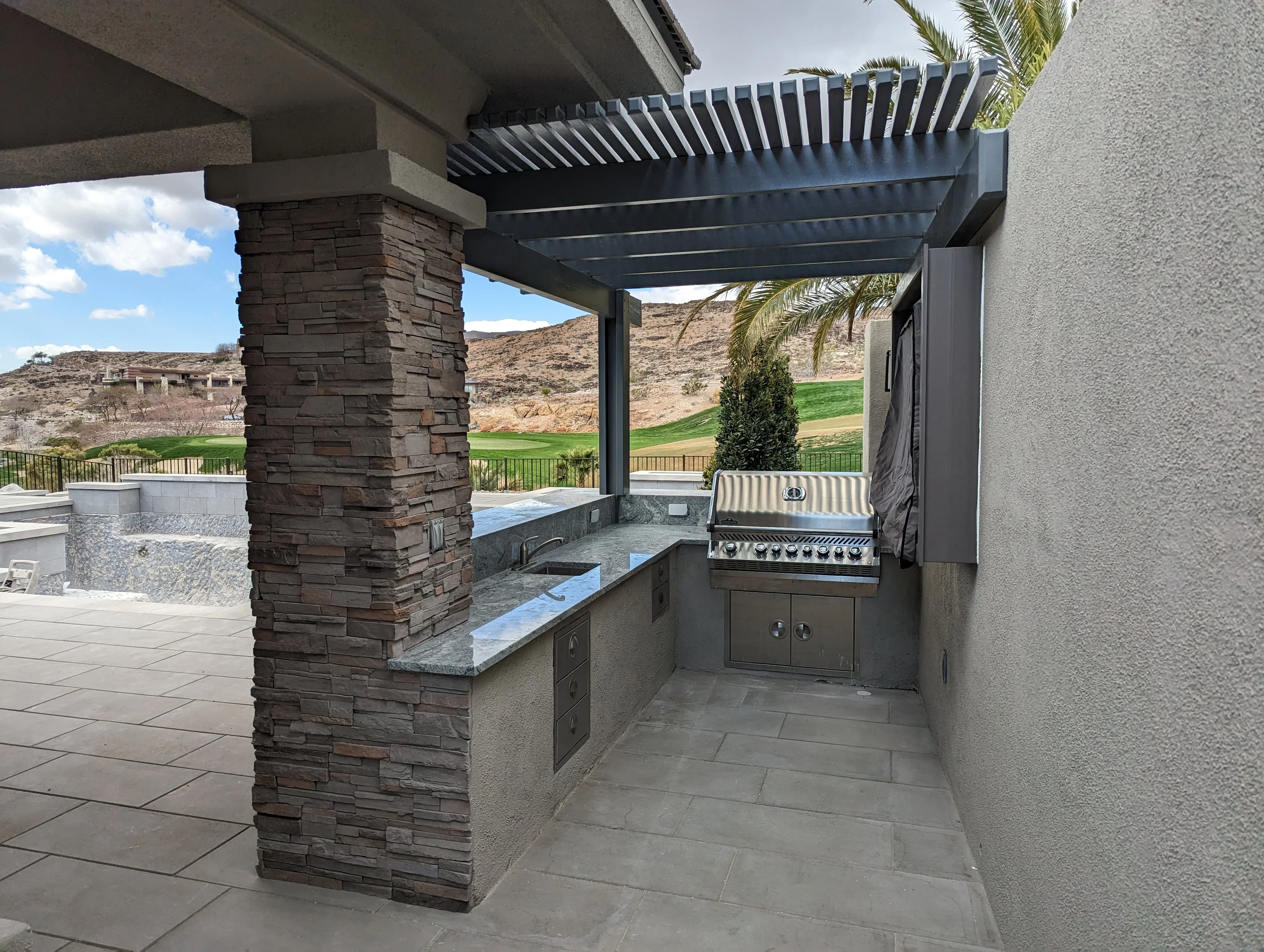 Modern outdoor kitchen with stone column, built-in grill, and black aluminum pergola