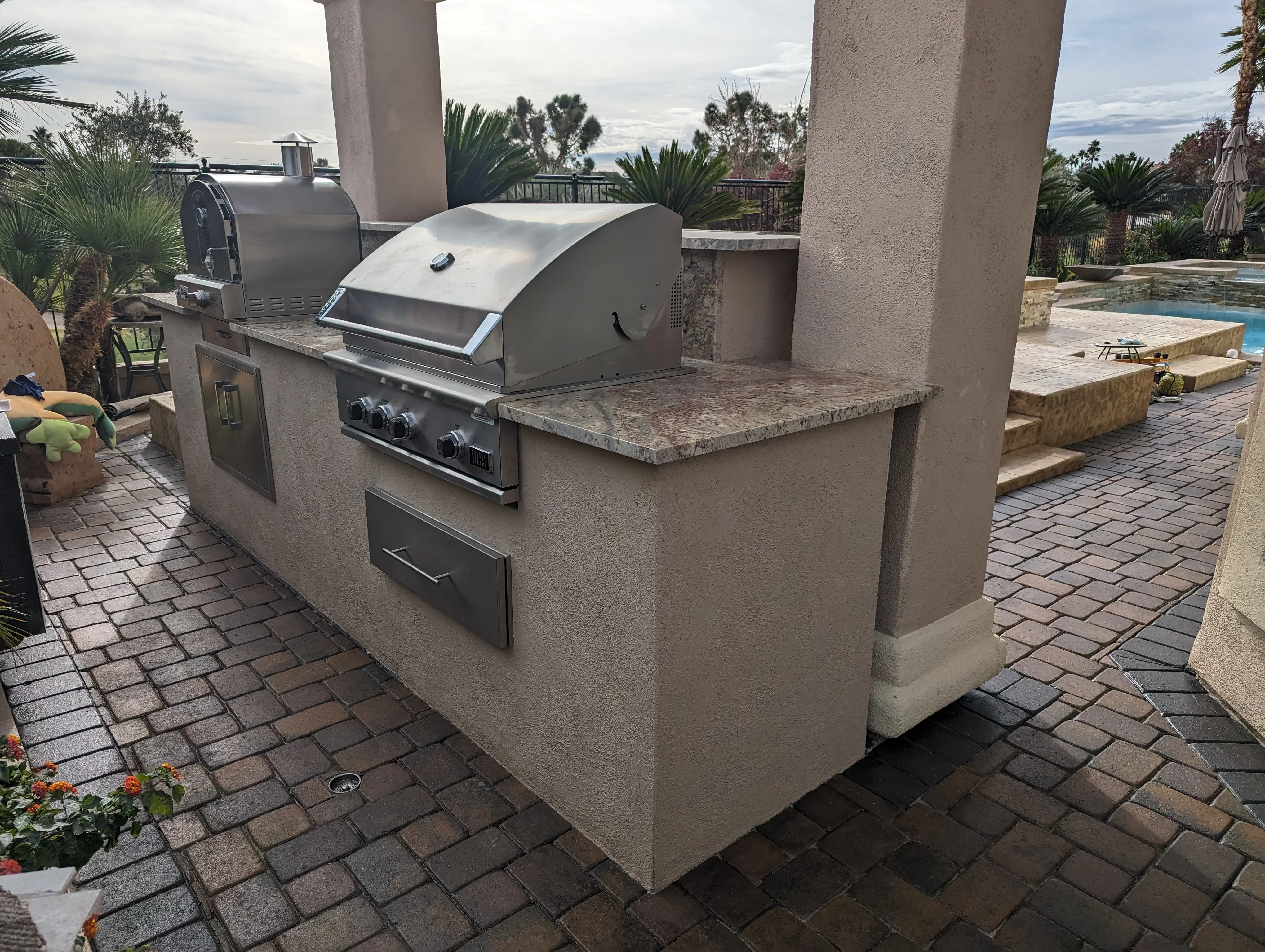 Stucco outdoor kitchen island with stainless steel grill and smoker on clay brick patio
