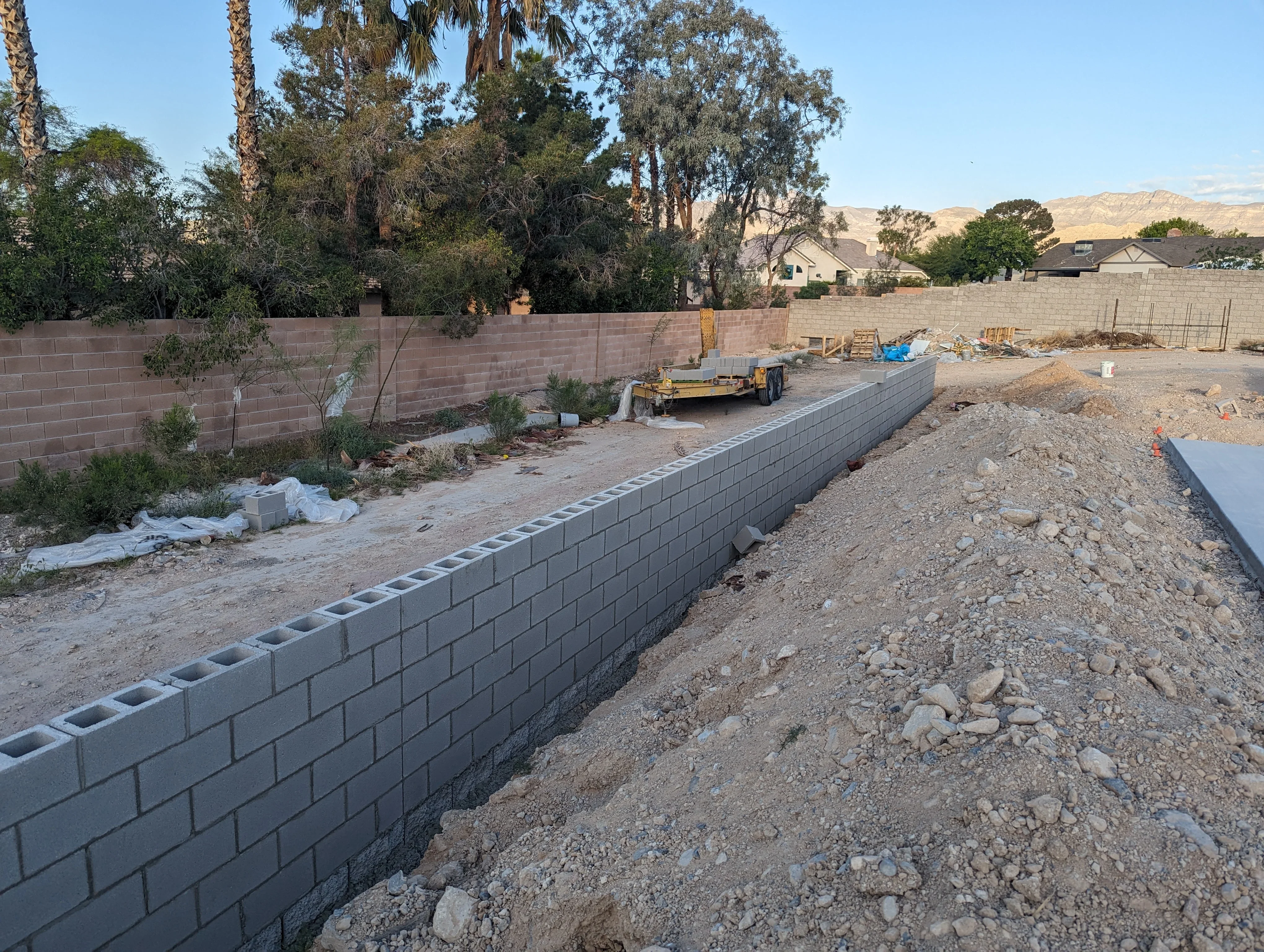 Concrete block retaining wall under construction with compacted soil base and surrounding landscape