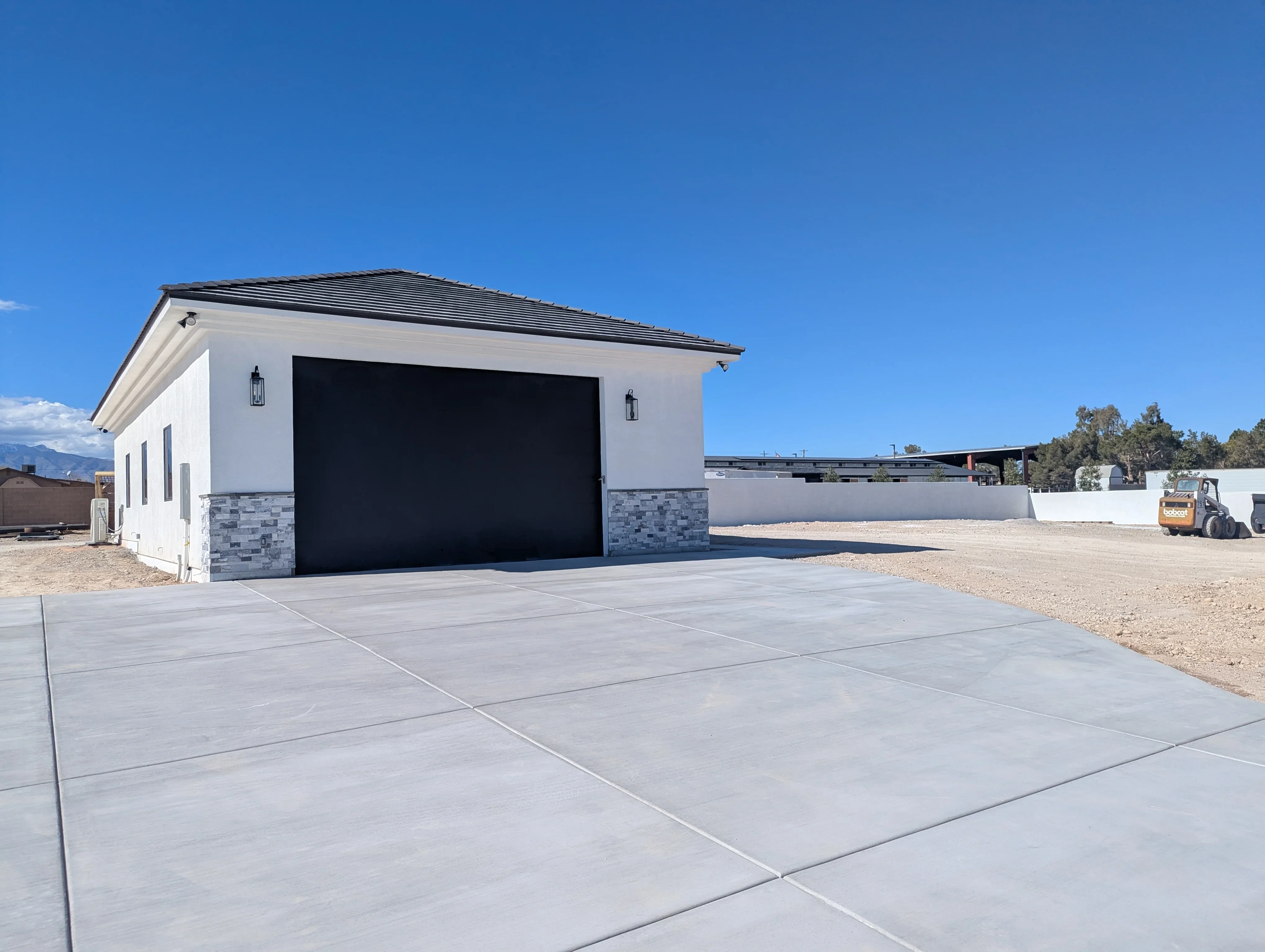 Modern white garage with black door and stone veneer base on finished concrete driveway