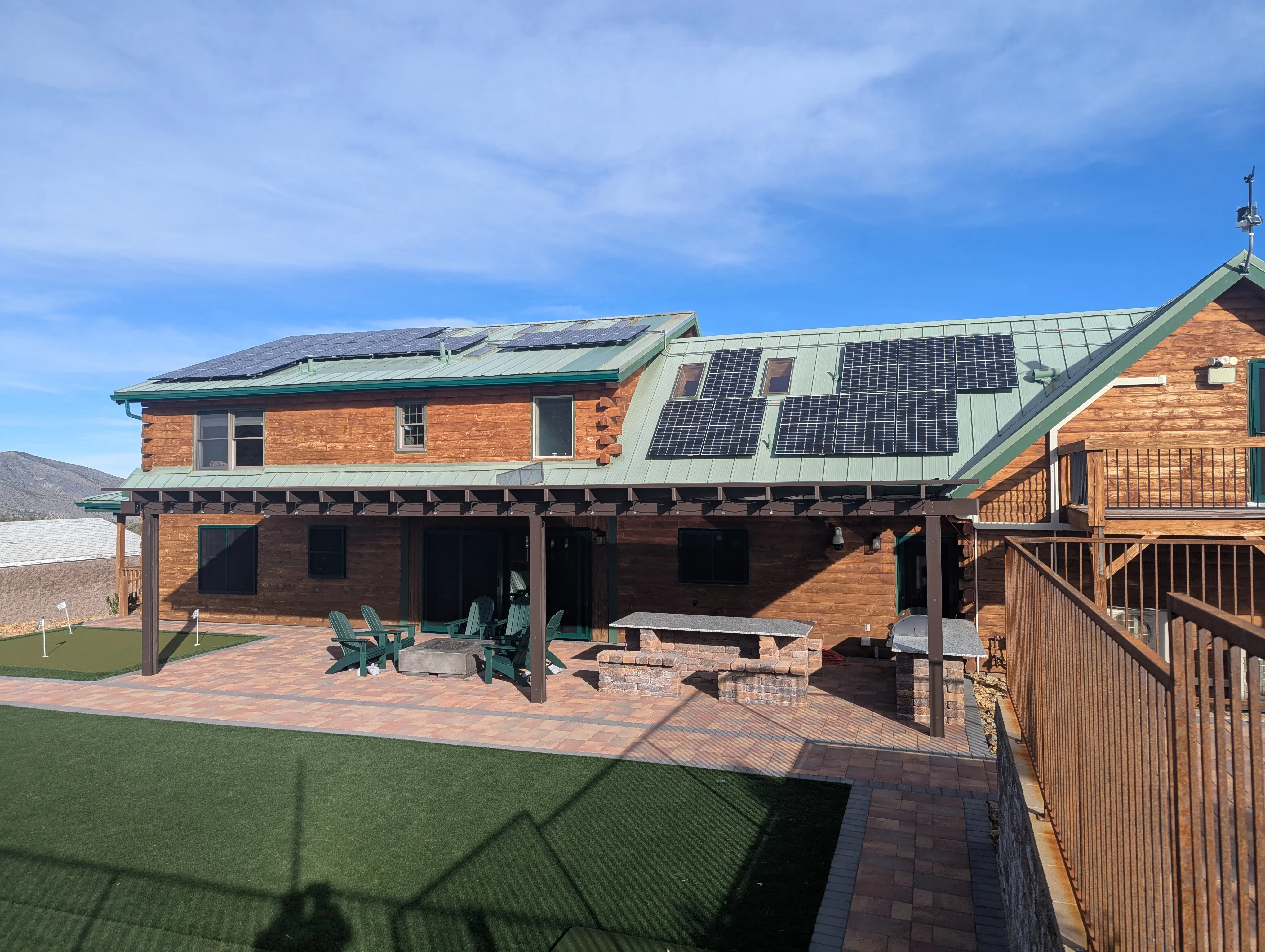 Brick patio with pergola, fire pit, and wooden deck attached to log home with solar panels