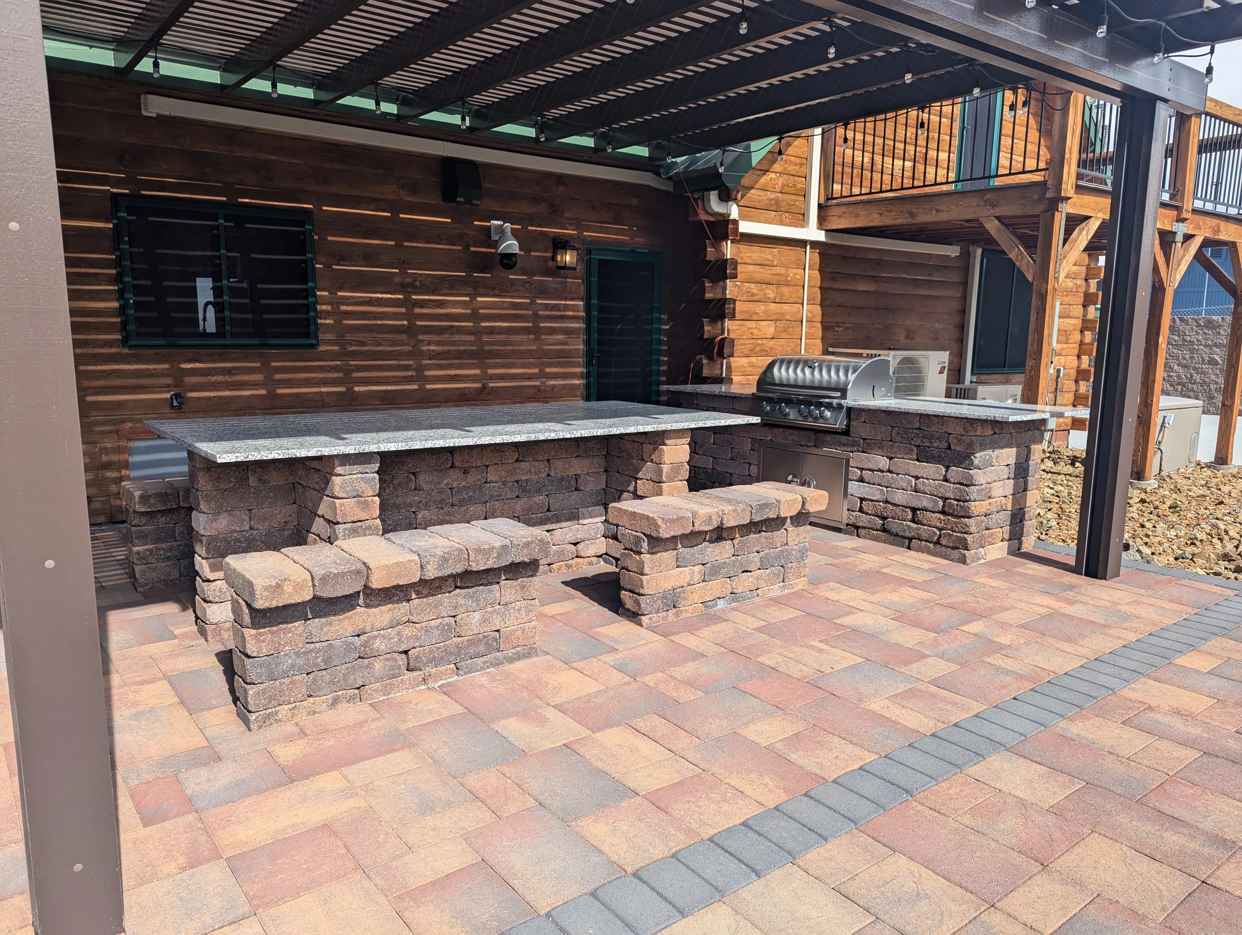 Brick patio with built-in seating, granite counters, and stainless steel grill under pergola