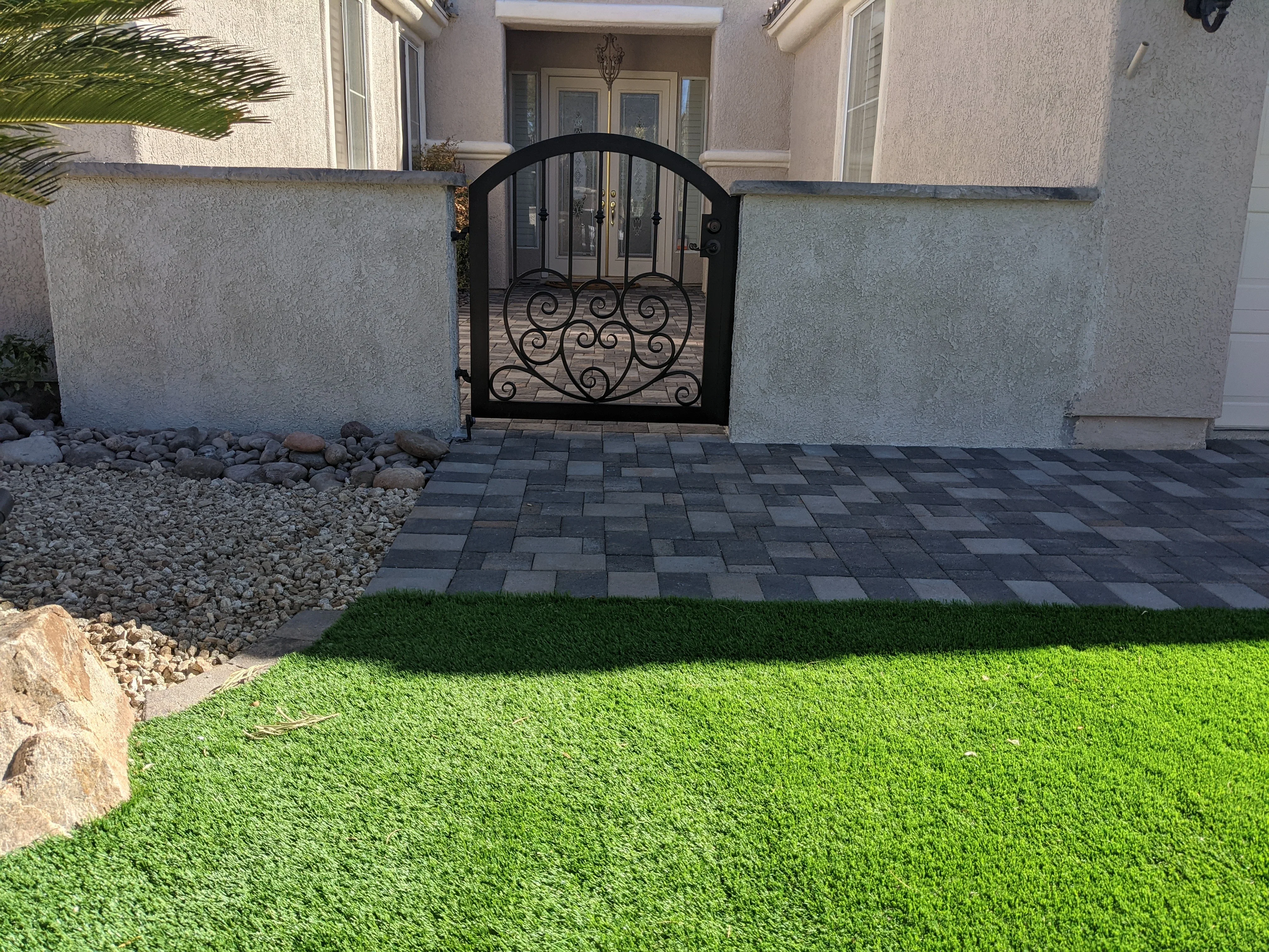 Front courtyard with dark paver patio, concrete walls, decorative iron gate, and synthetic turf