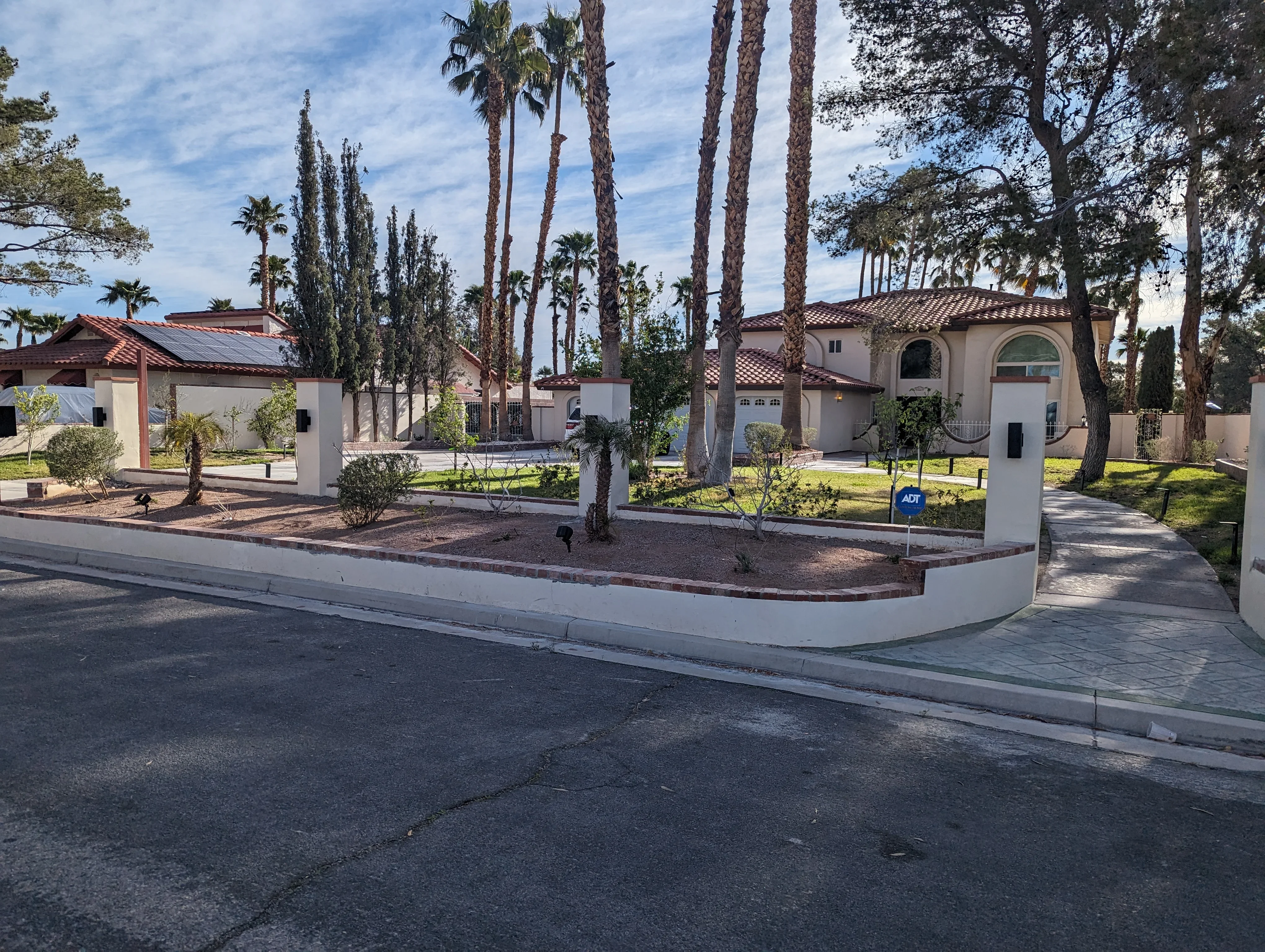 Curved concrete driveway entry with white stucco pillars and mature palms at Mediterranean-style estate
