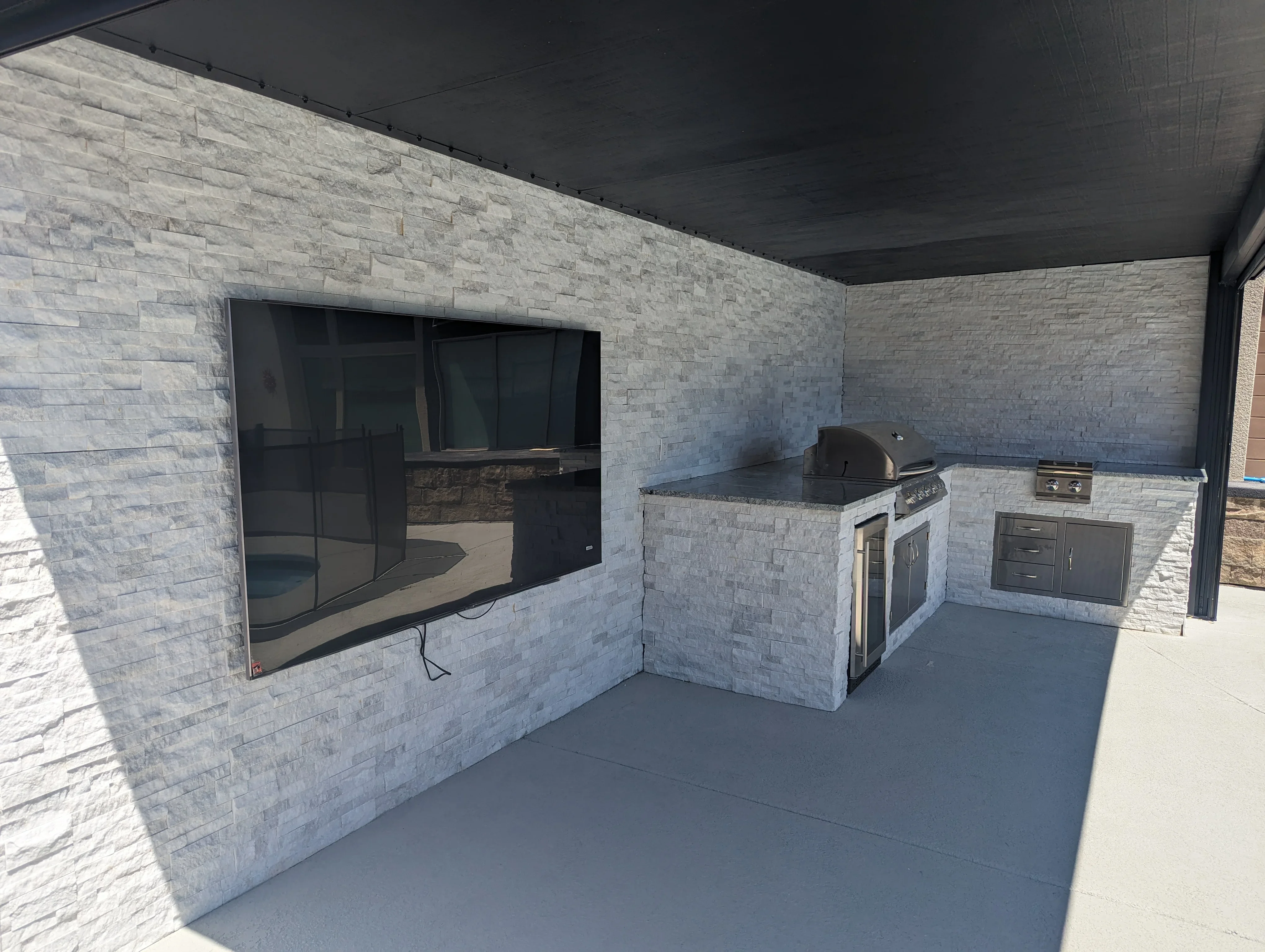 Modern patio with stone veneer walls, built-in grill, and covered seating area