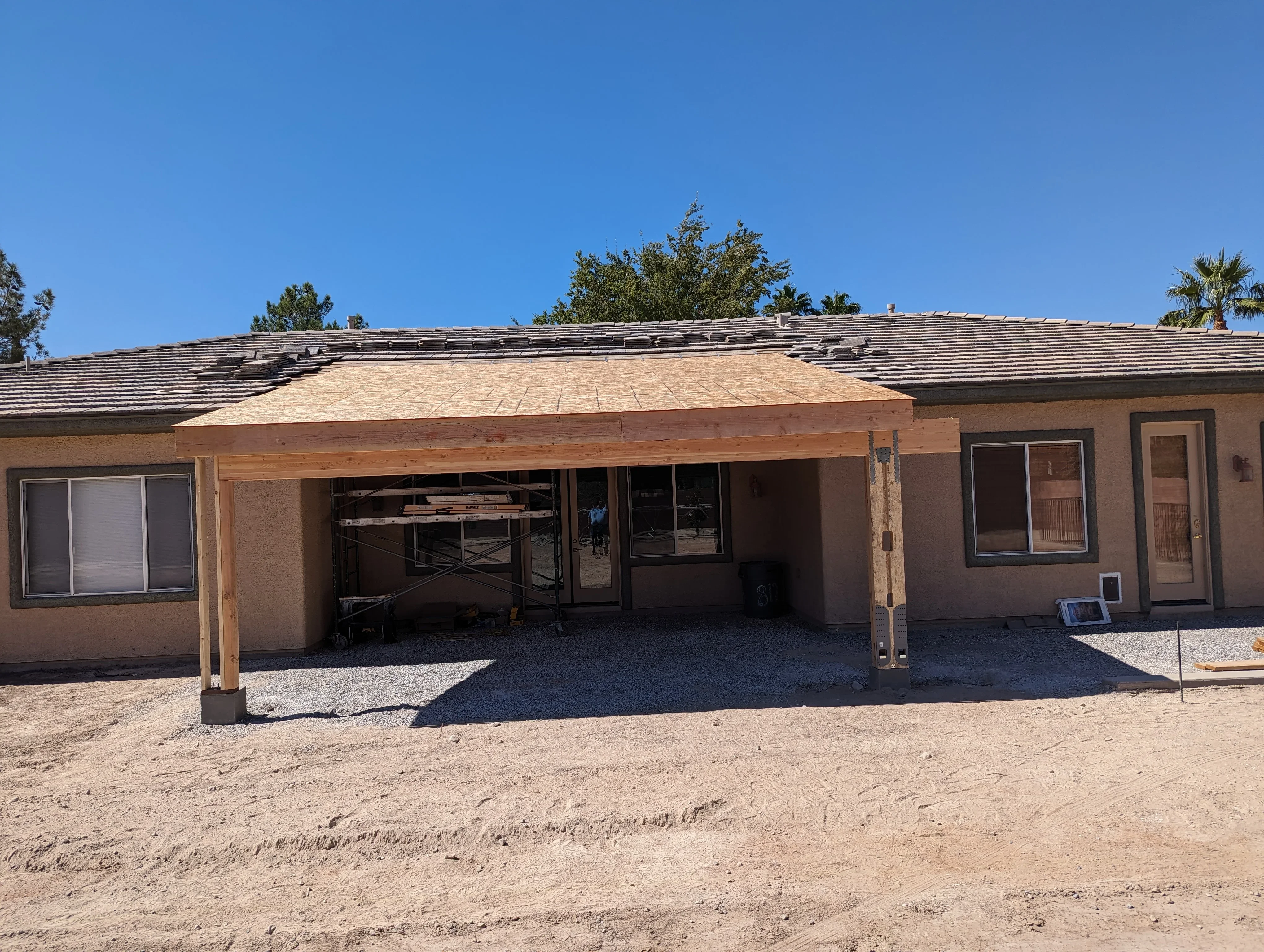 Wood patio cover with composite roof attached to brick home in desert setting