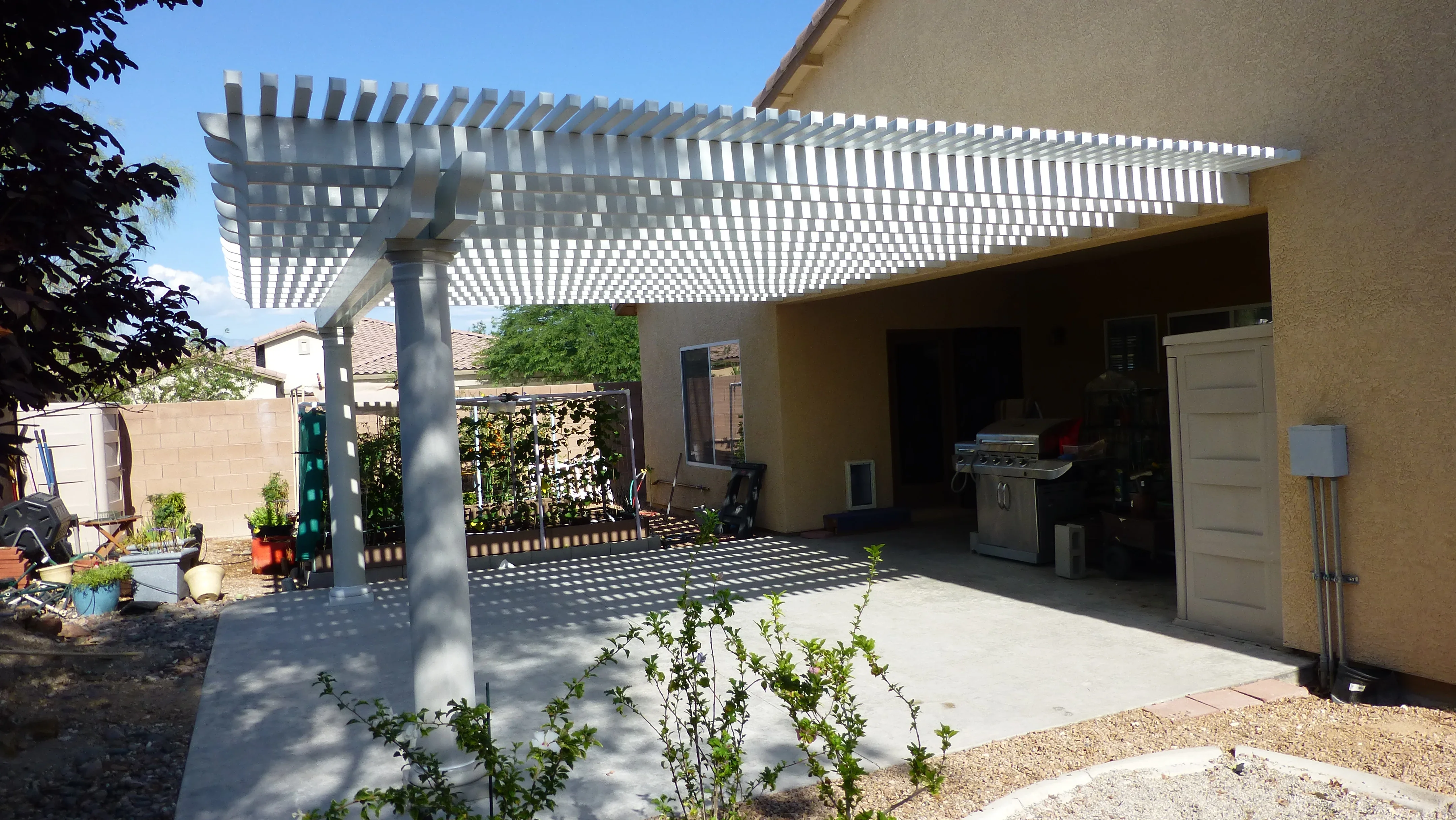 White aluminum pergola with lattice panels over concrete patio beside tan stucco home