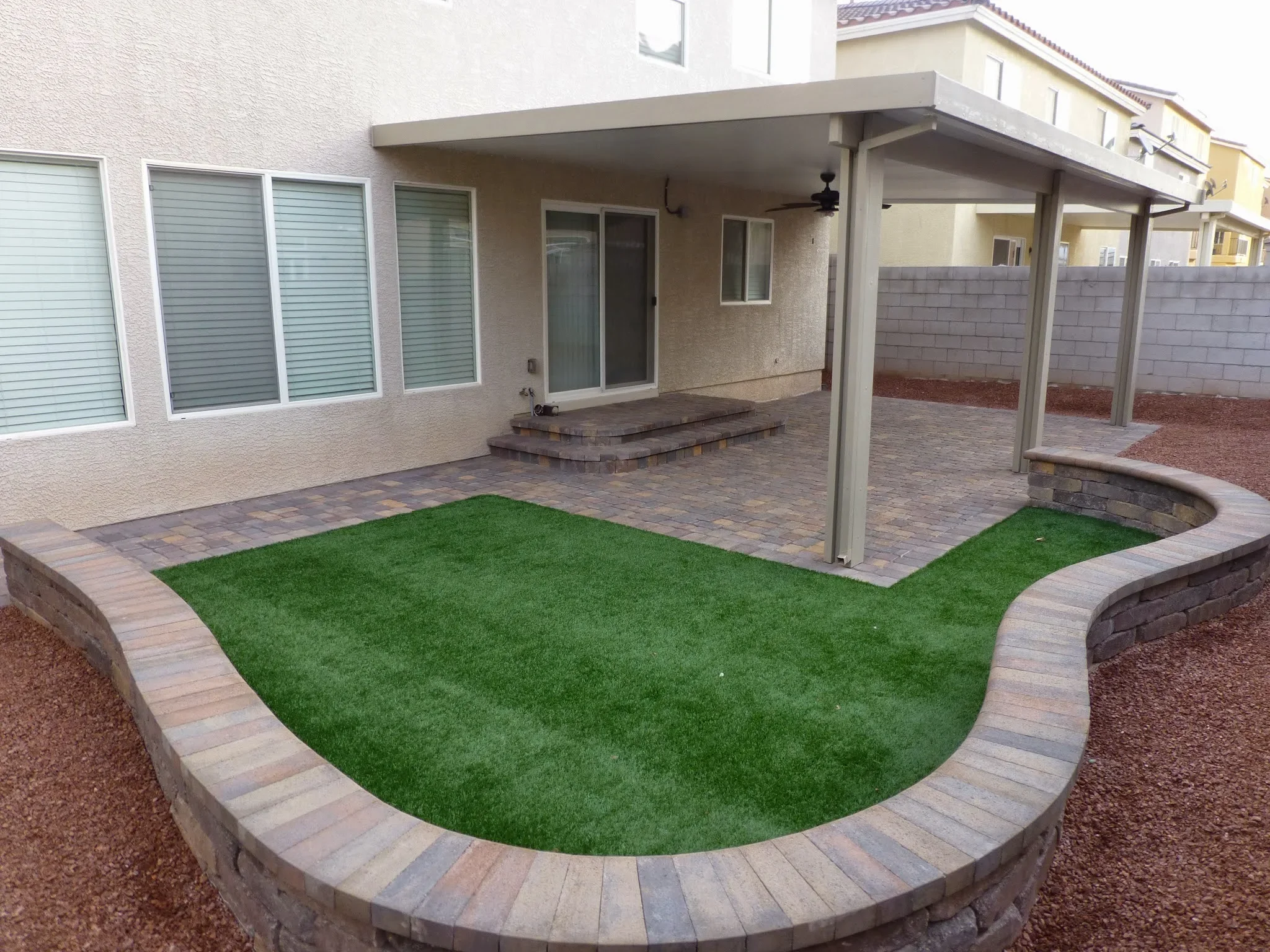 Patio with pavers, artificial grass, pergola, and curved retaining walls in Las Vegas