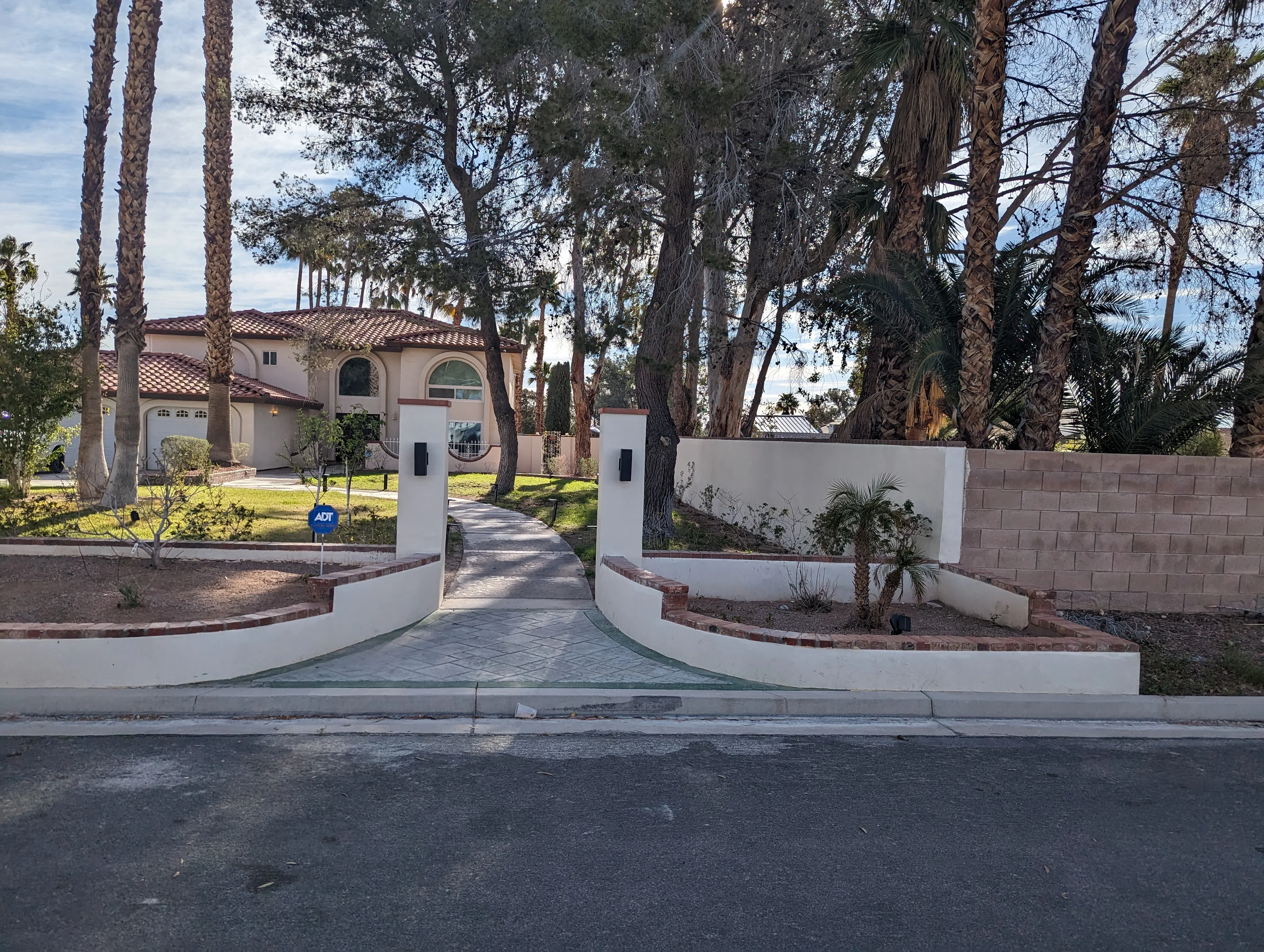 Curved white stucco entry gates with brick trim and geometric paver driveway