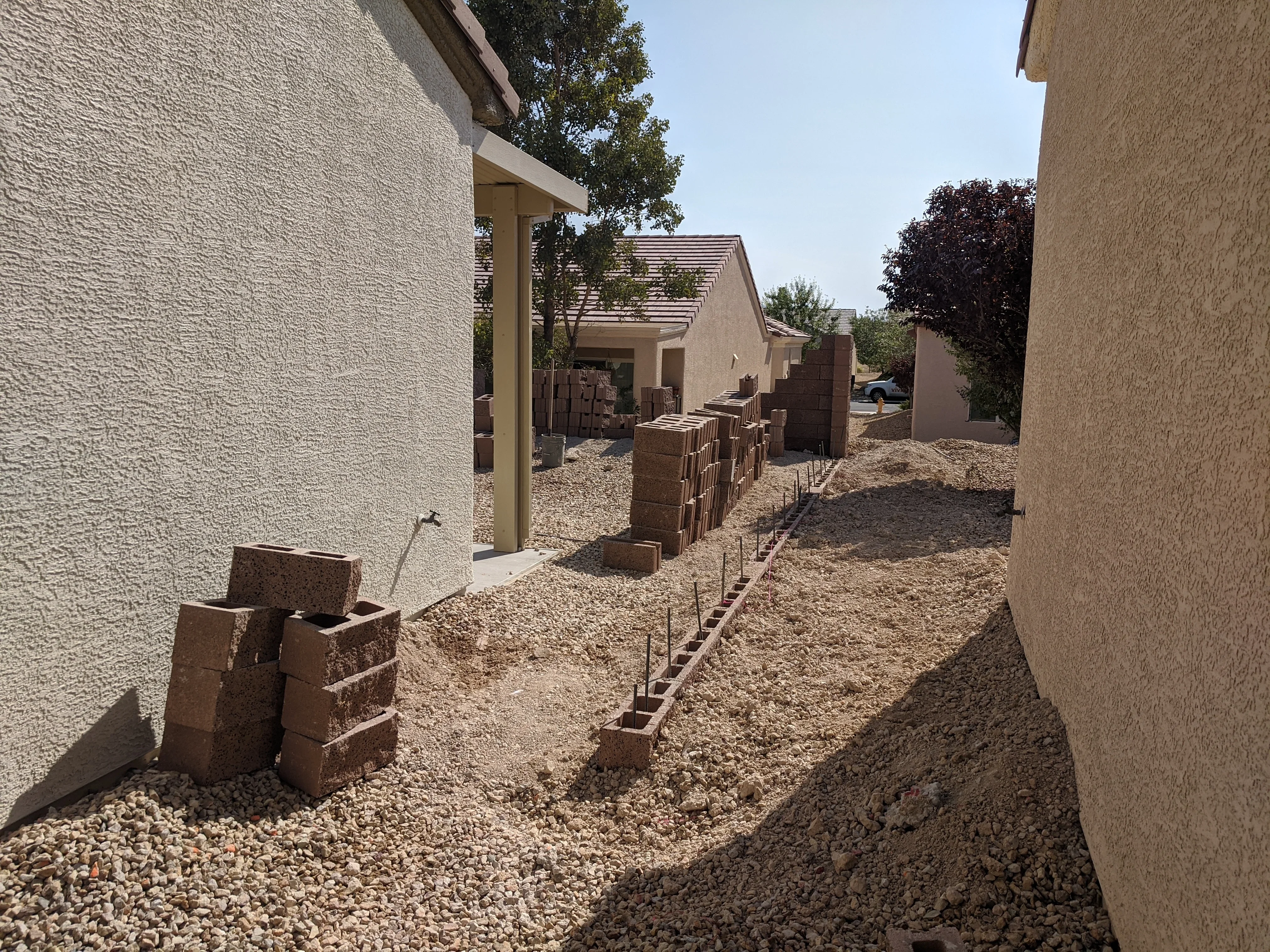 Residential hardscape project with brick retaining walls, gravel pathways, and metal edging between homes