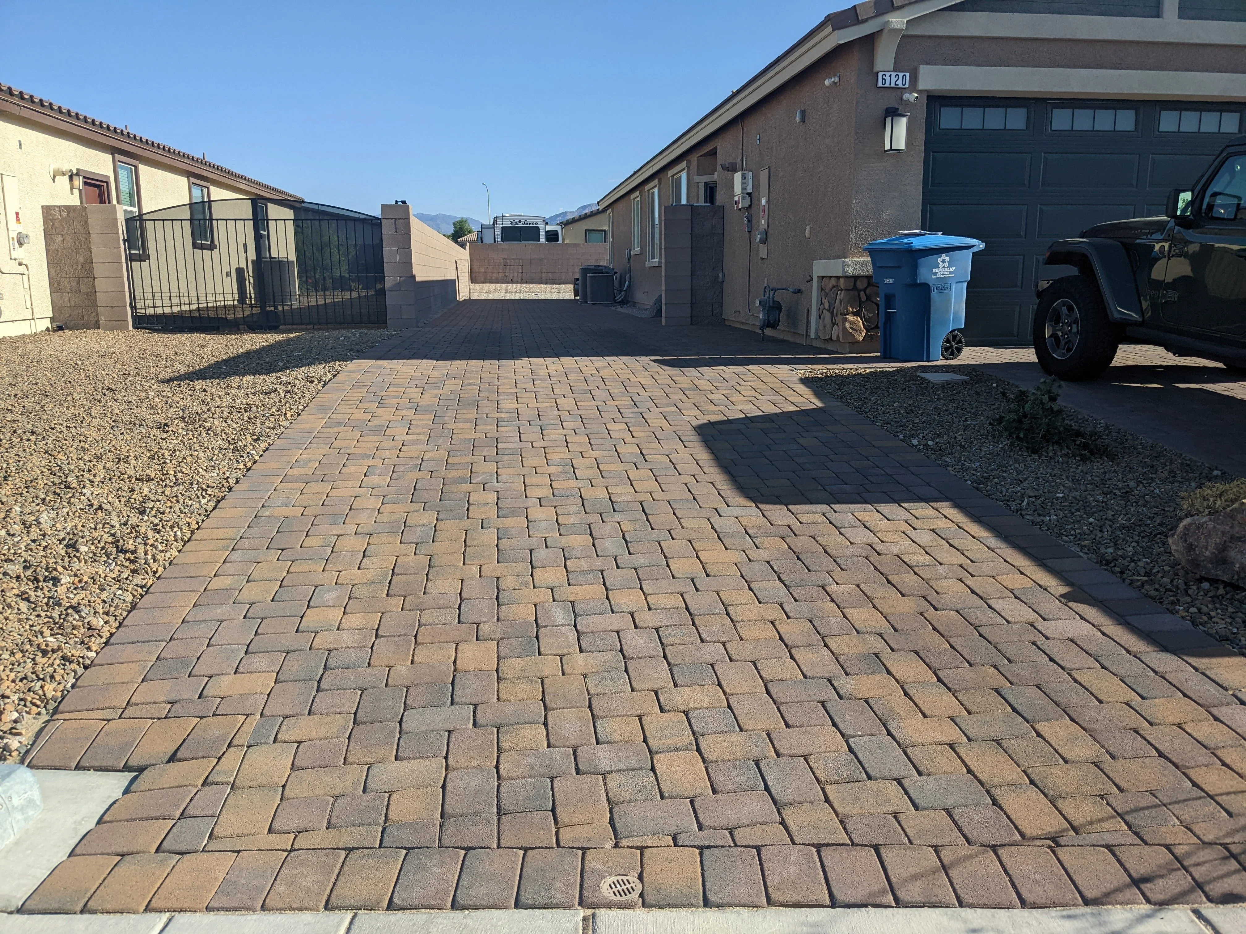 Clay brick paver driveway in herringbone pattern with metal gate and gravel borders