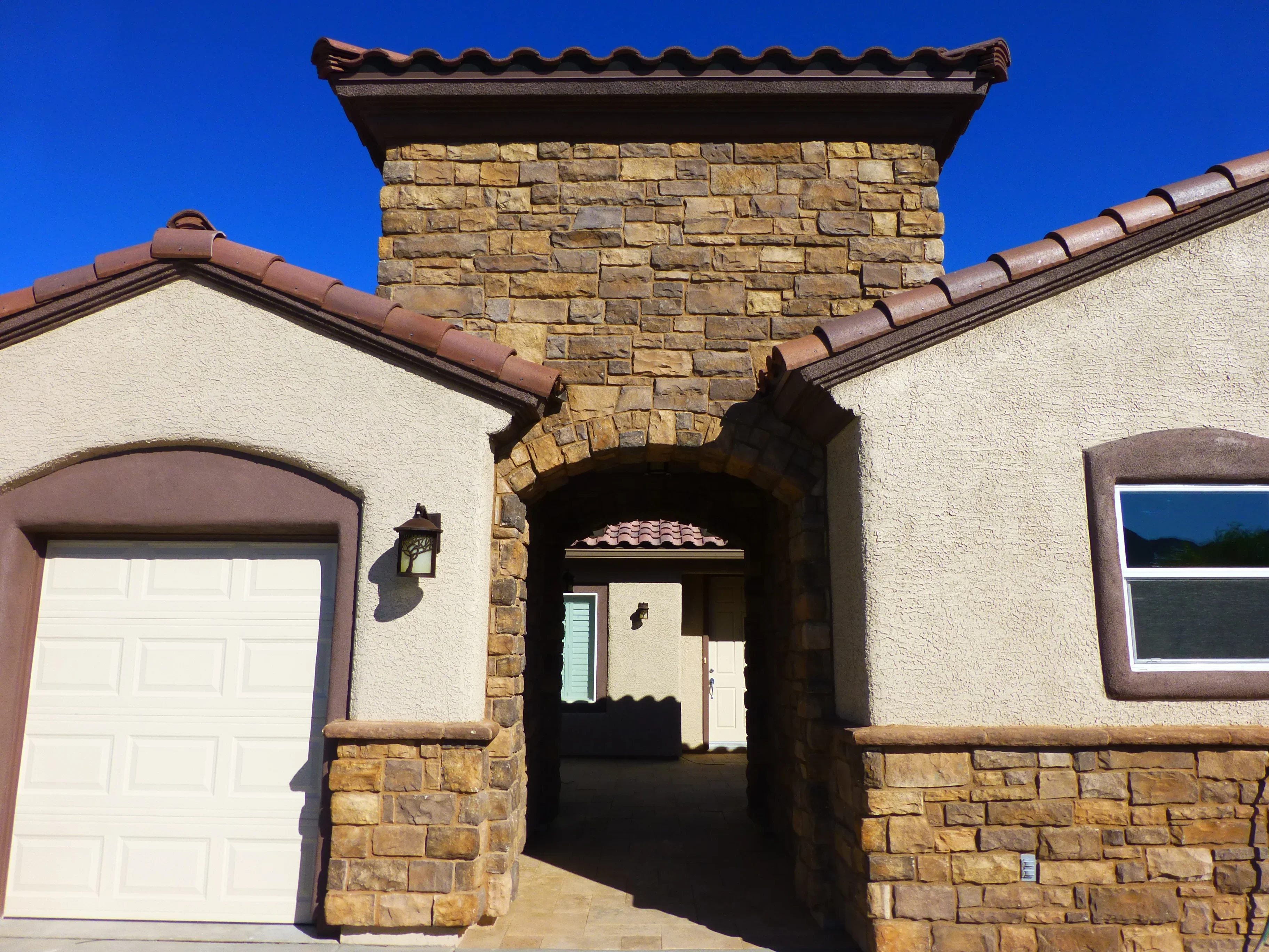 Stone chimney with decorative cap and arched entryway on stucco home with clay tile roof