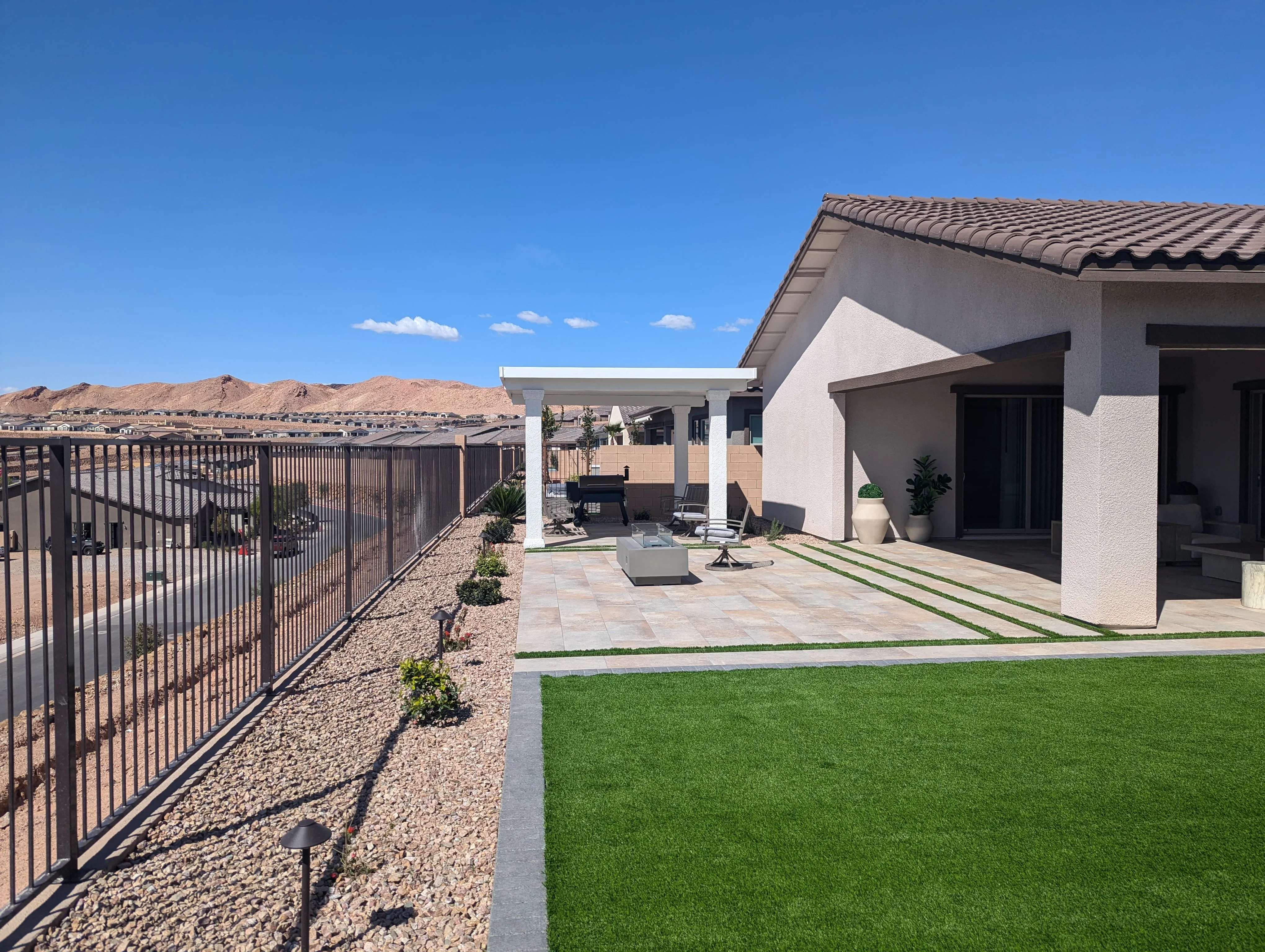 Modern patio with white pergola, clay tile pavers, synthetic turf, and fire pit in Las Vegas
