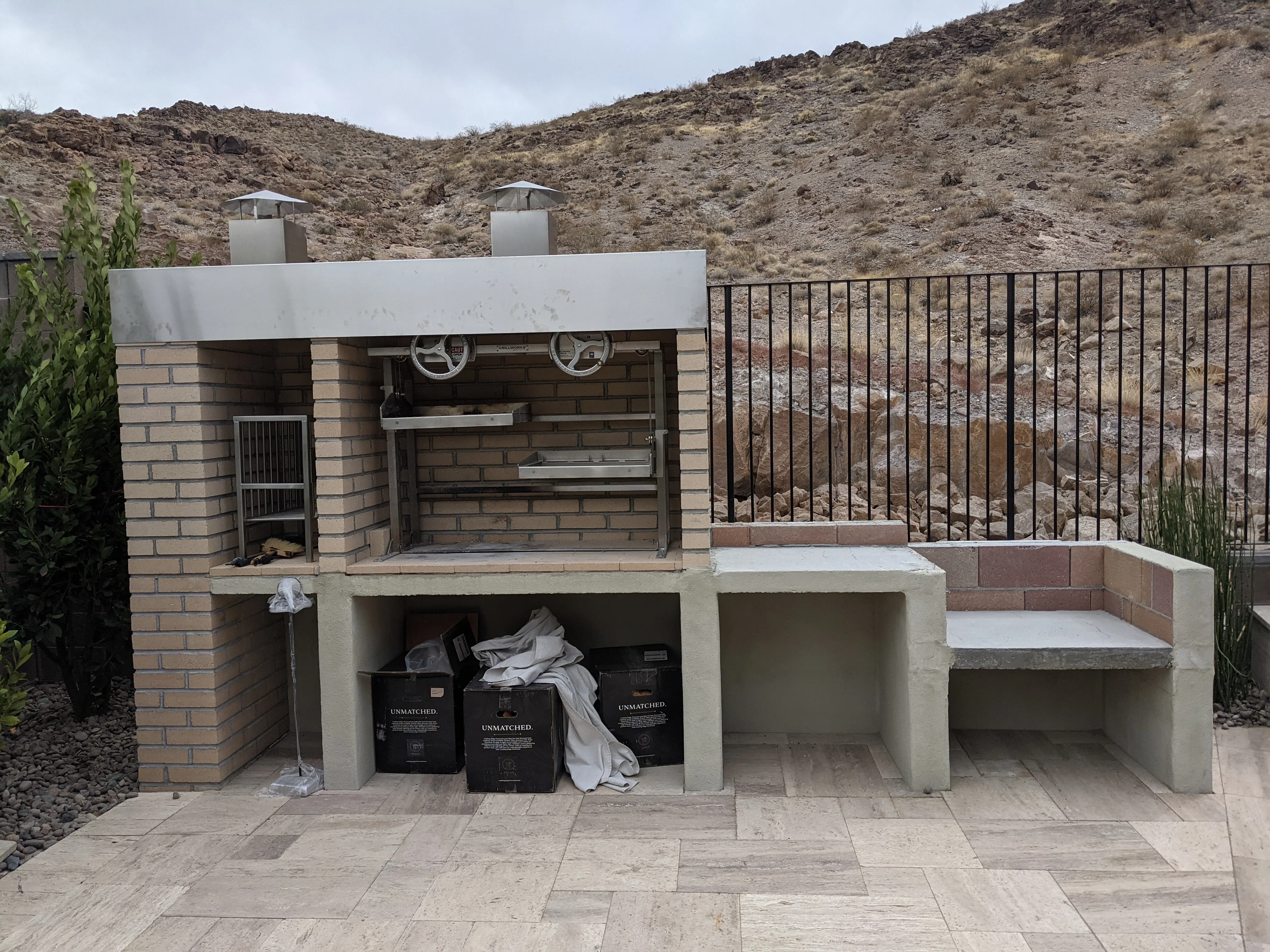 Custom outdoor kitchen with brick construction, grill, and metal railing on paver patio