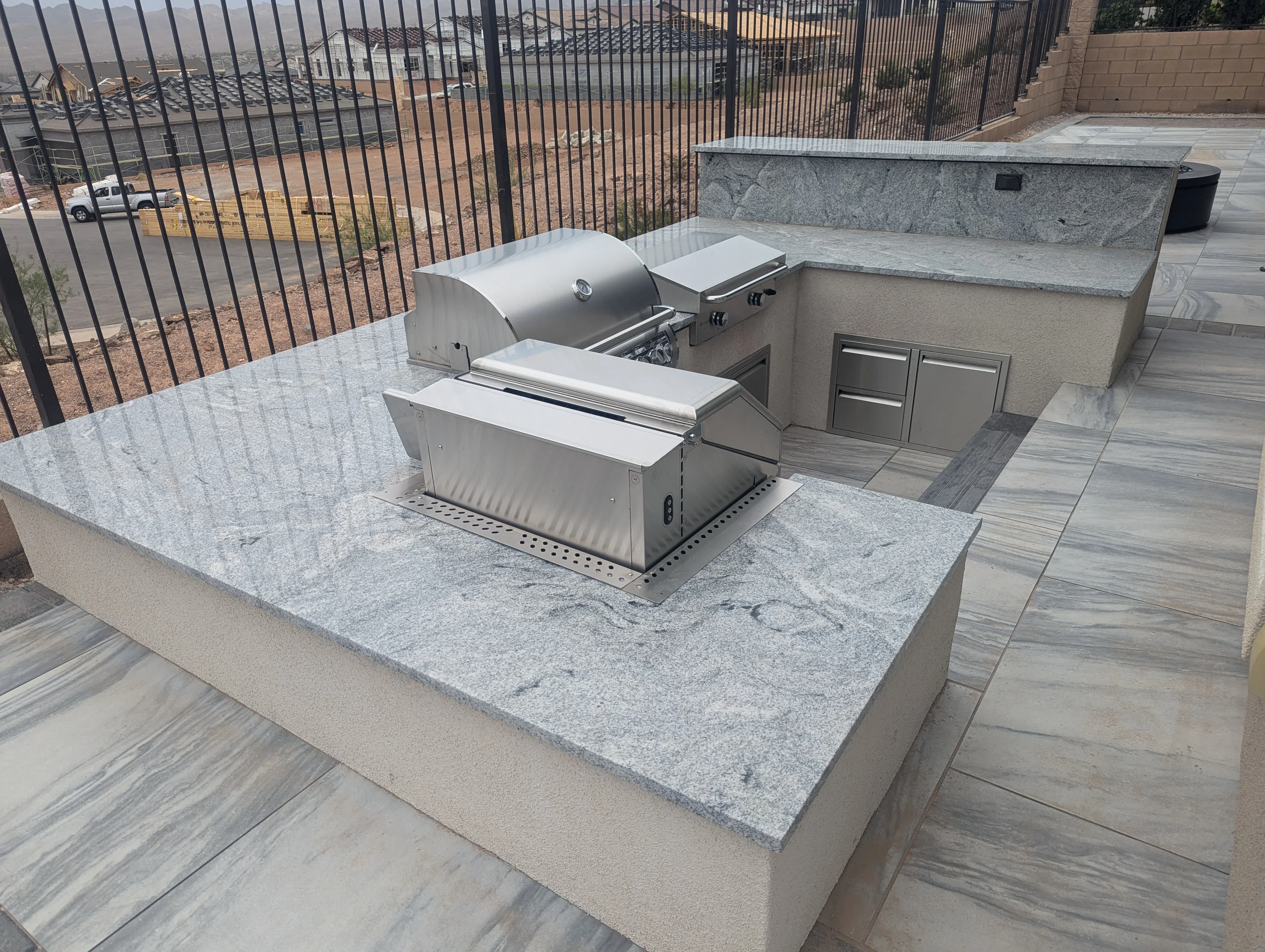 Outdoor kitchen island with stainless steel grill, granite countertop, and storage cabinets on composite deck