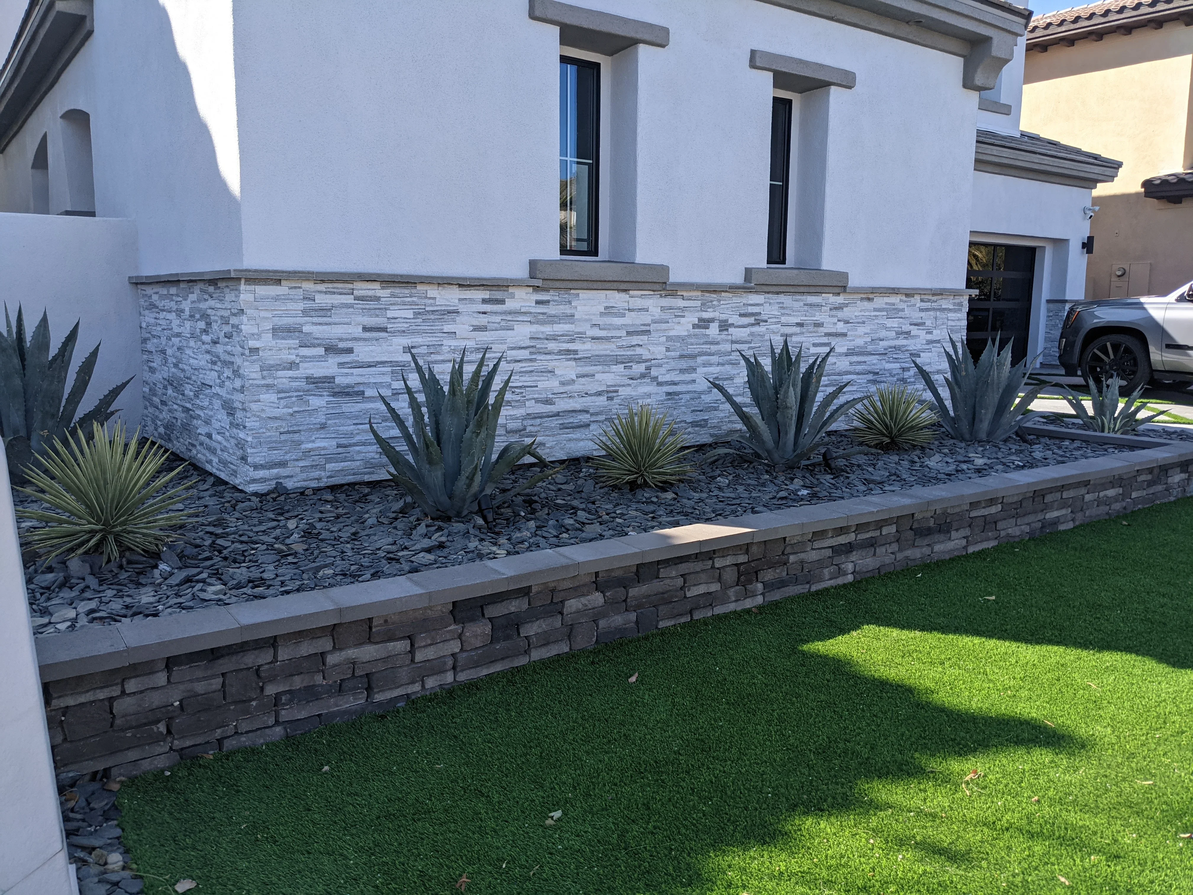 Modern front yard with stacked stone veneer planter, agave plants, and river rock landscaping