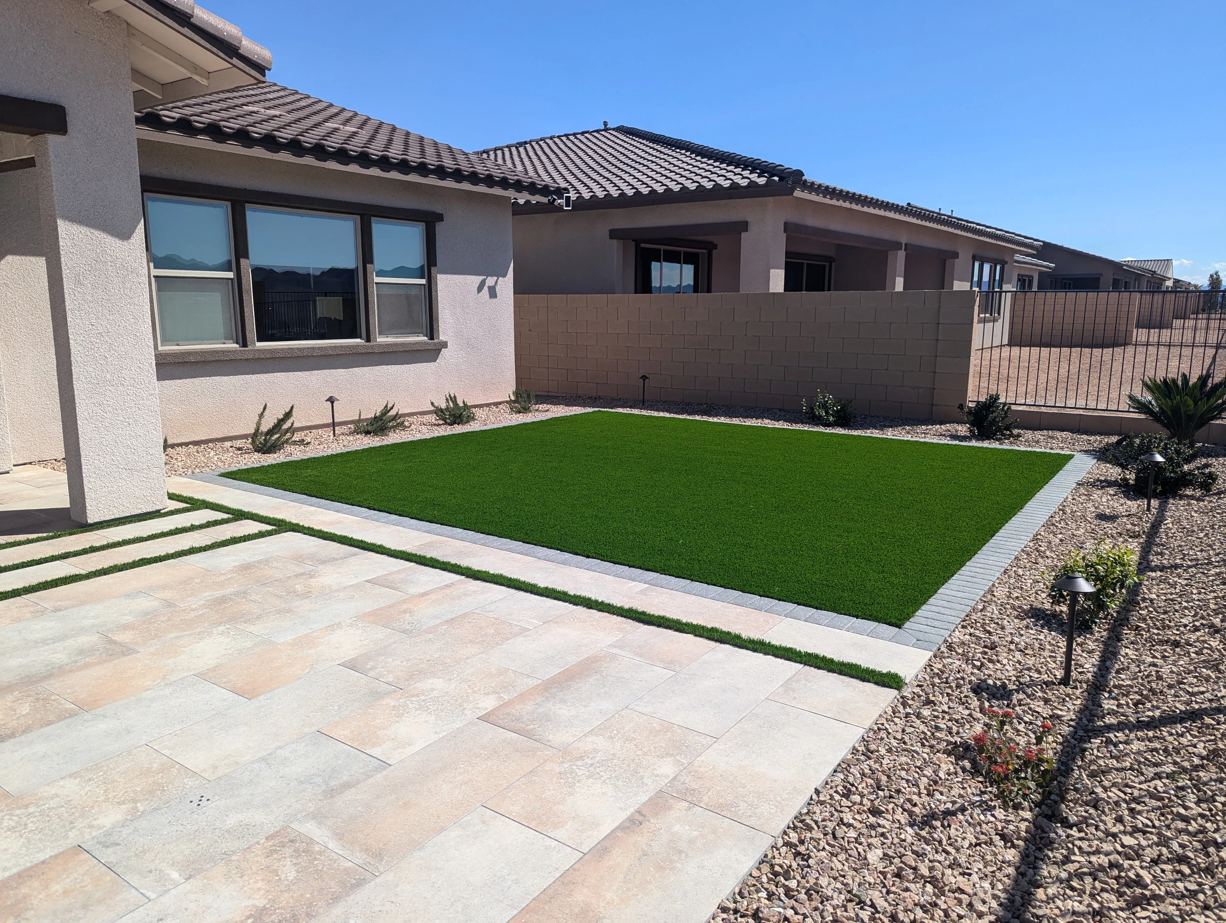 Modern patio with synthetic turf, concrete pavers, and desert landscaping against contemporary home