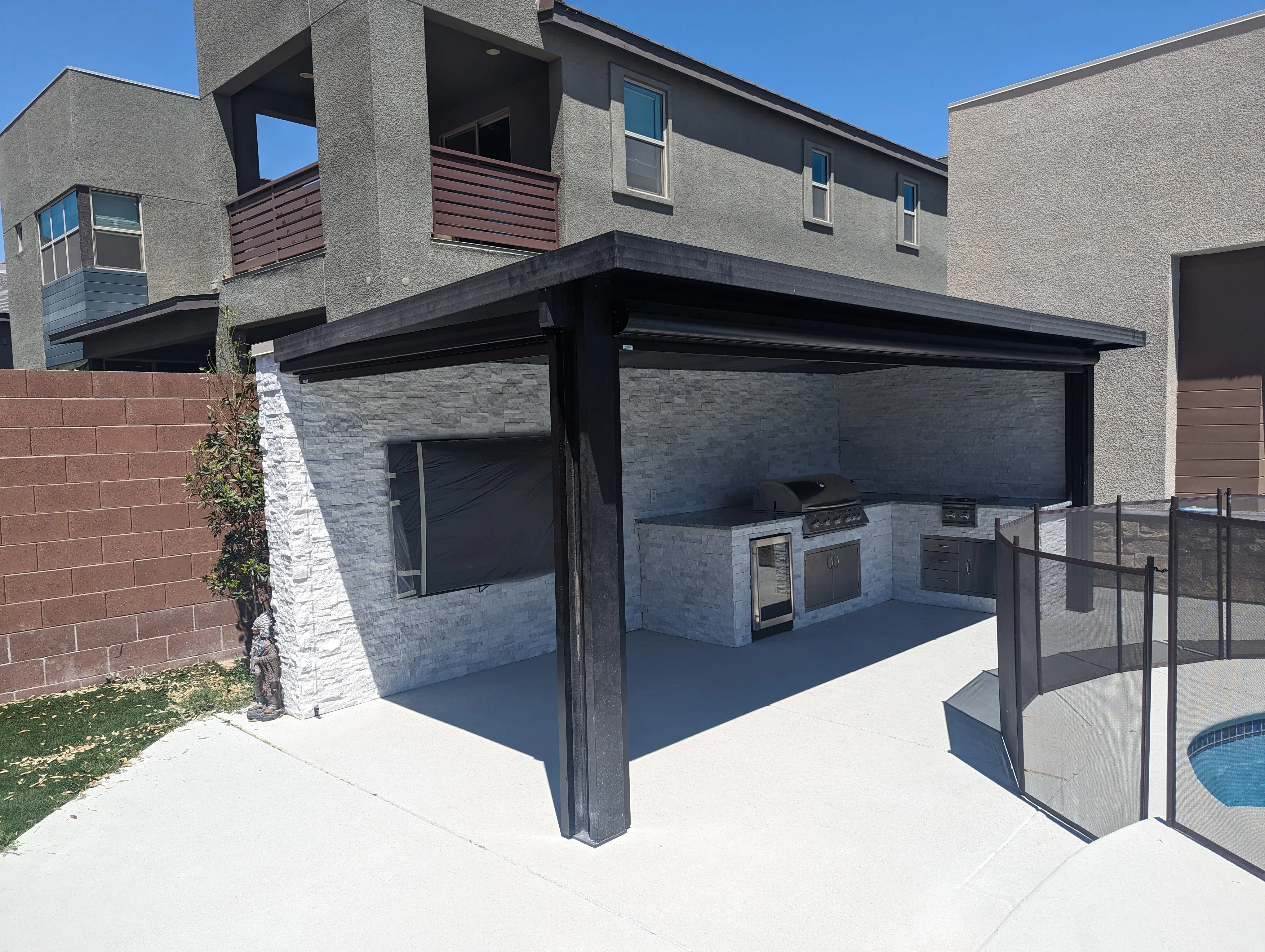 Modern patio with black pergola, outdoor kitchen appliances, and stone finishes