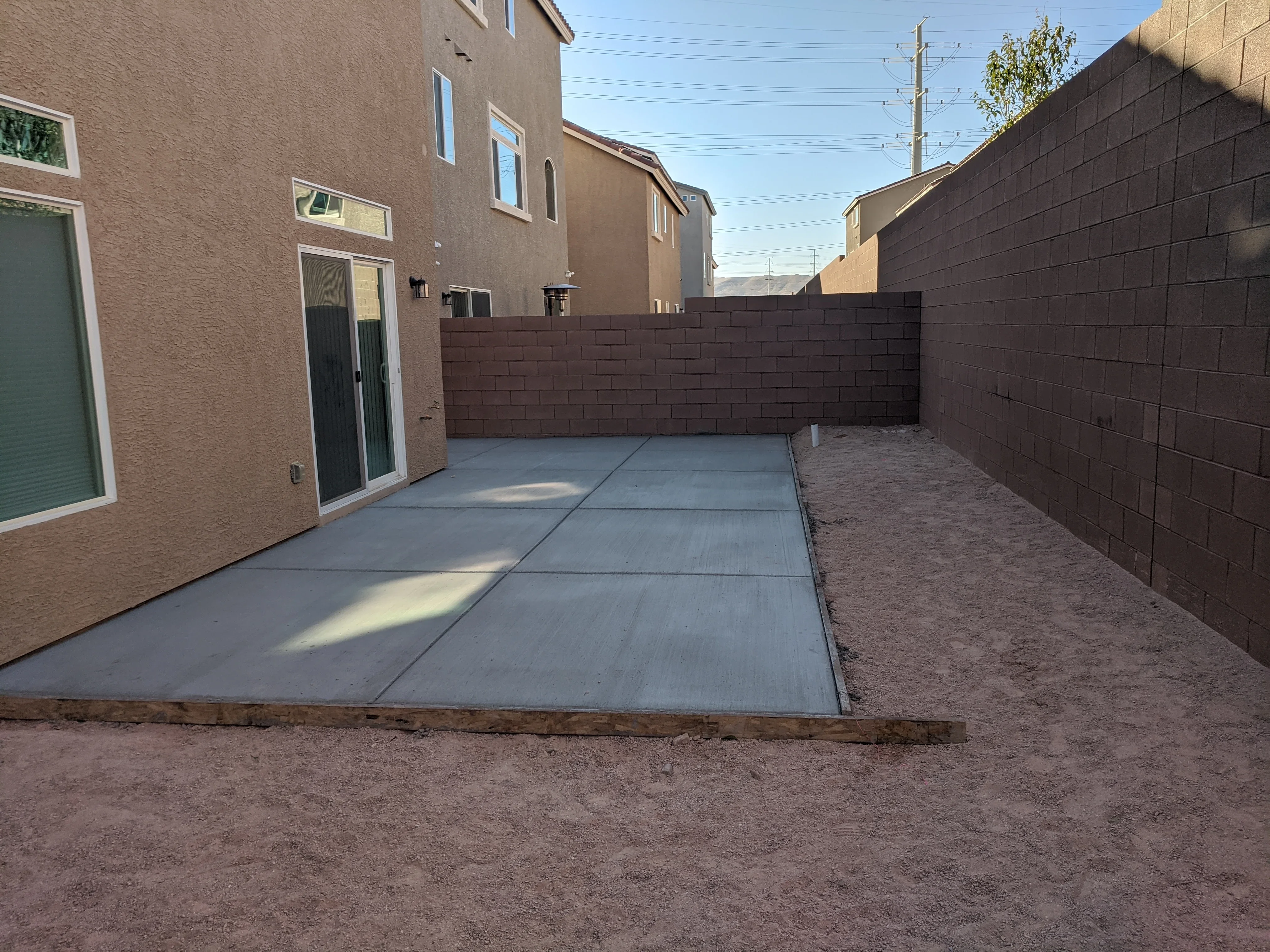 Concrete patio with control joints and brown block perimeter walls in residential backyard