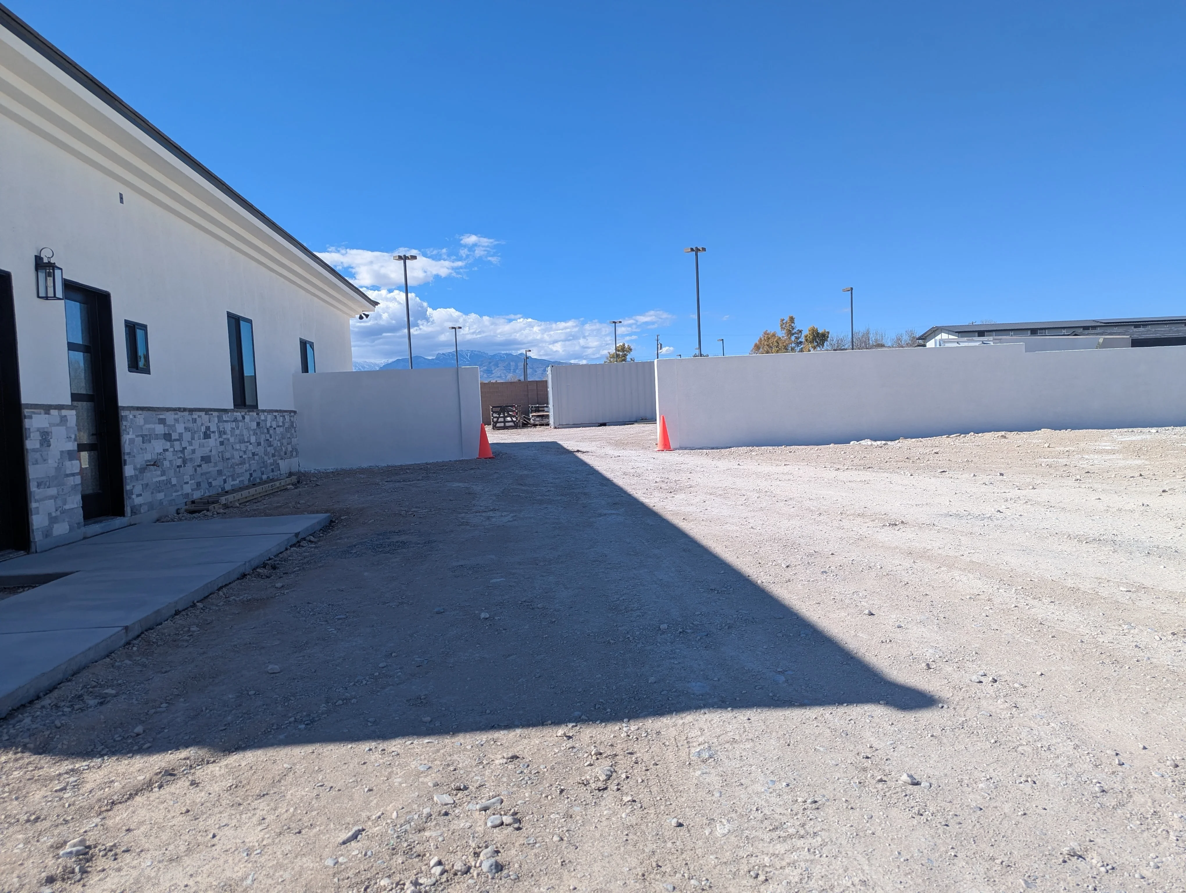 Commercial asphalt driveway with white building, perimeter fencing, and gravel site preparation