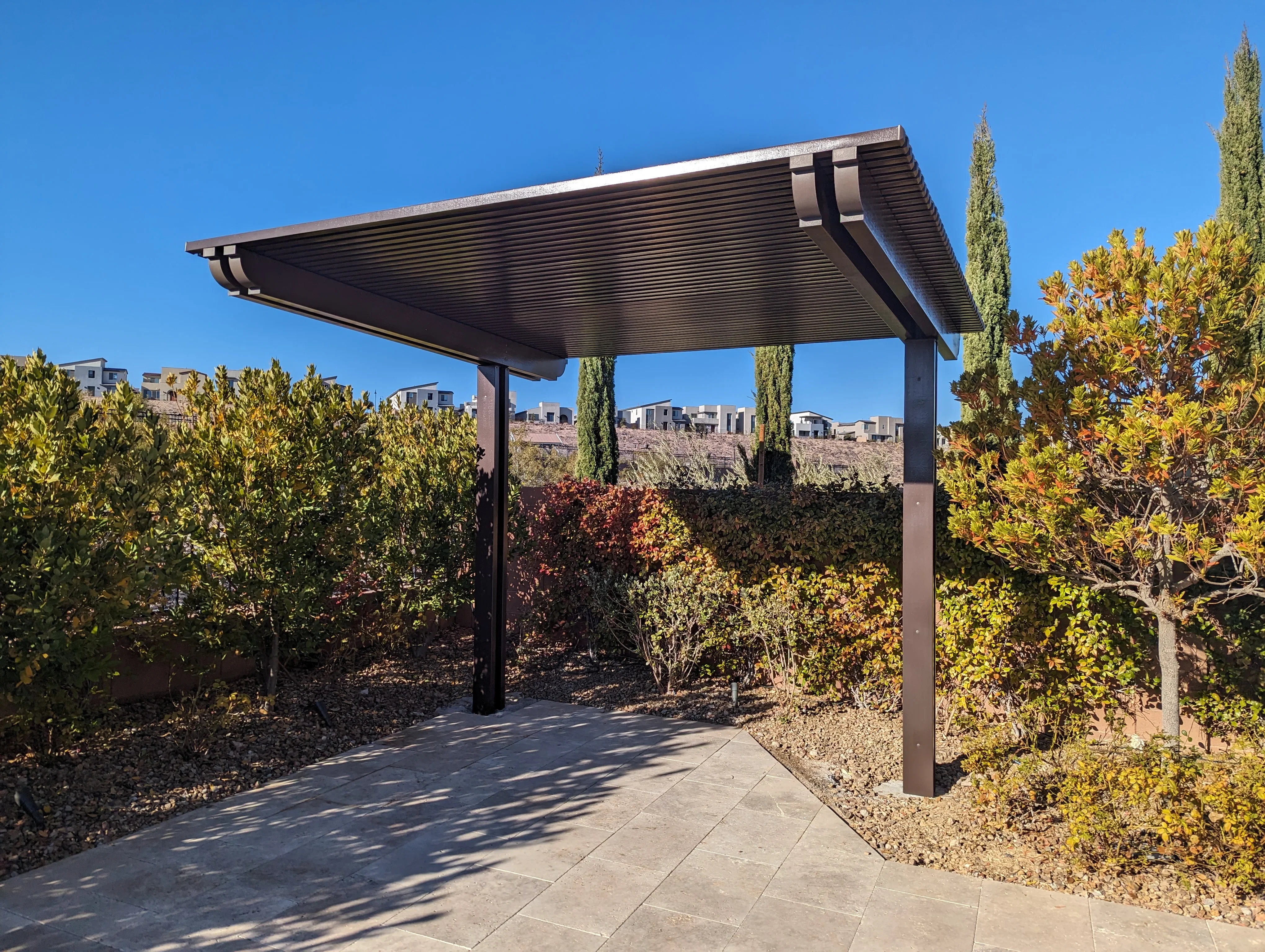 Modern black pergola with motorized louver roof over concrete patio in desert landscape