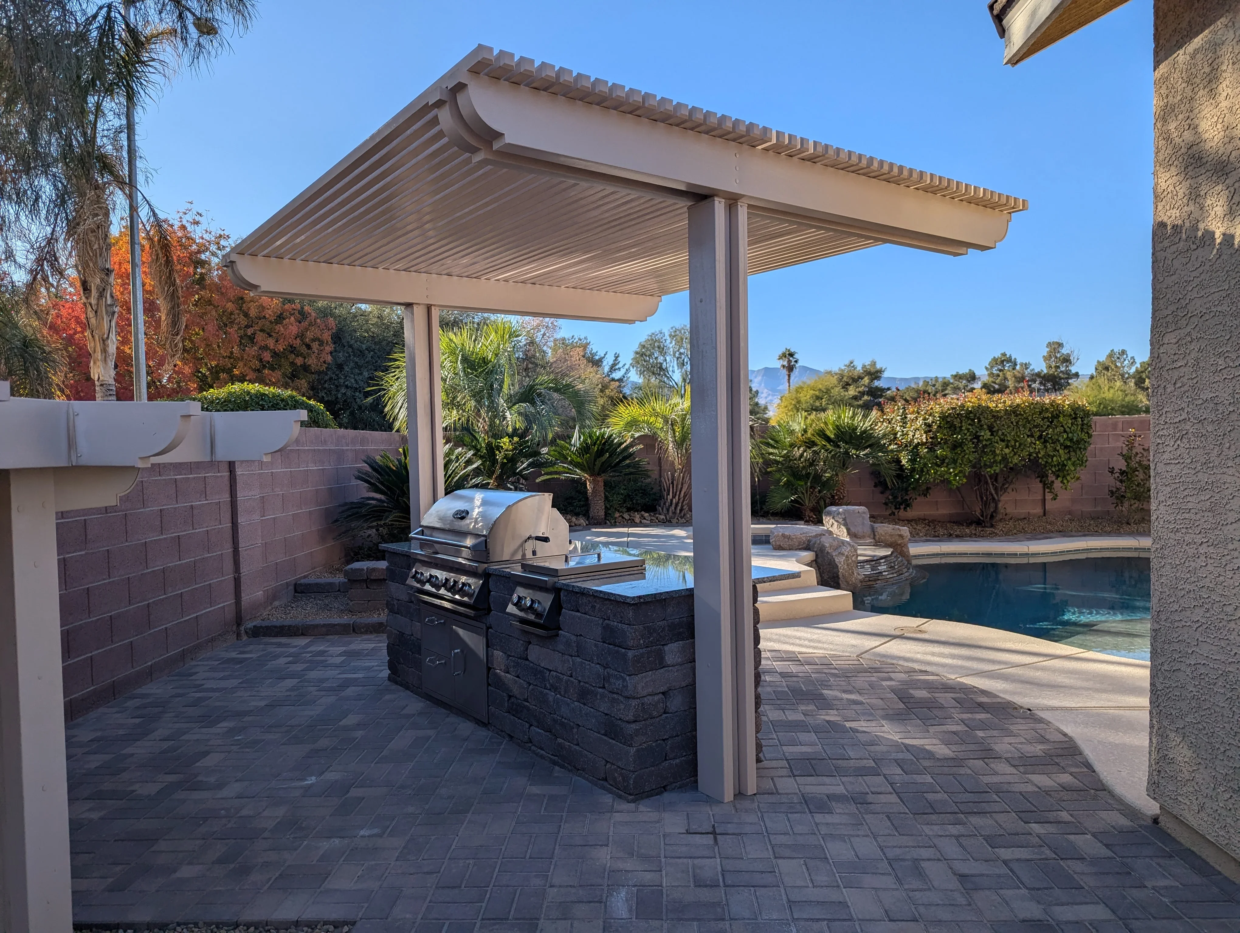 Modern pergola with louvered roof over paver patio and built-in outdoor kitchen grill