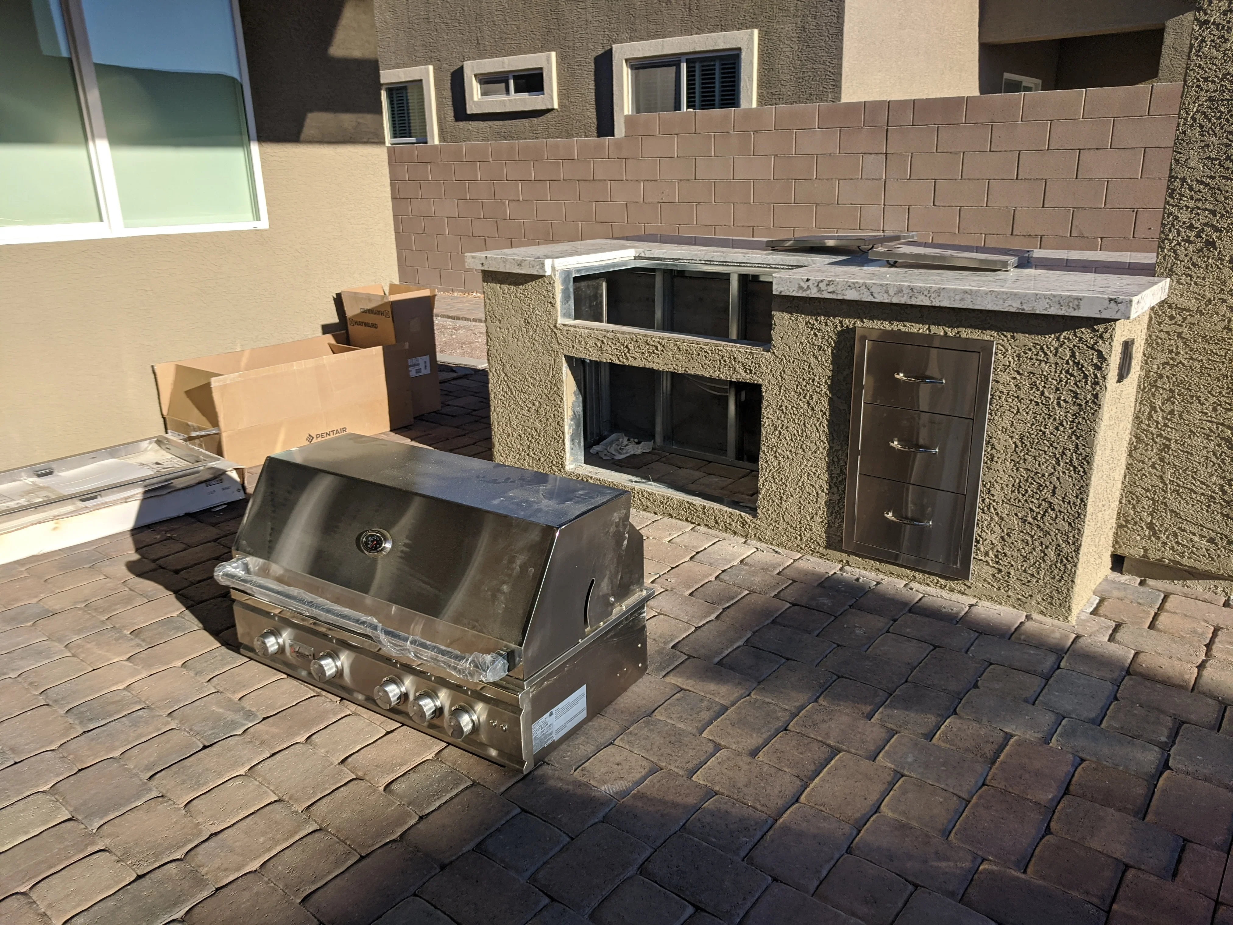 Outdoor kitchen island with stainless grill, stucco finish, and paver patio
