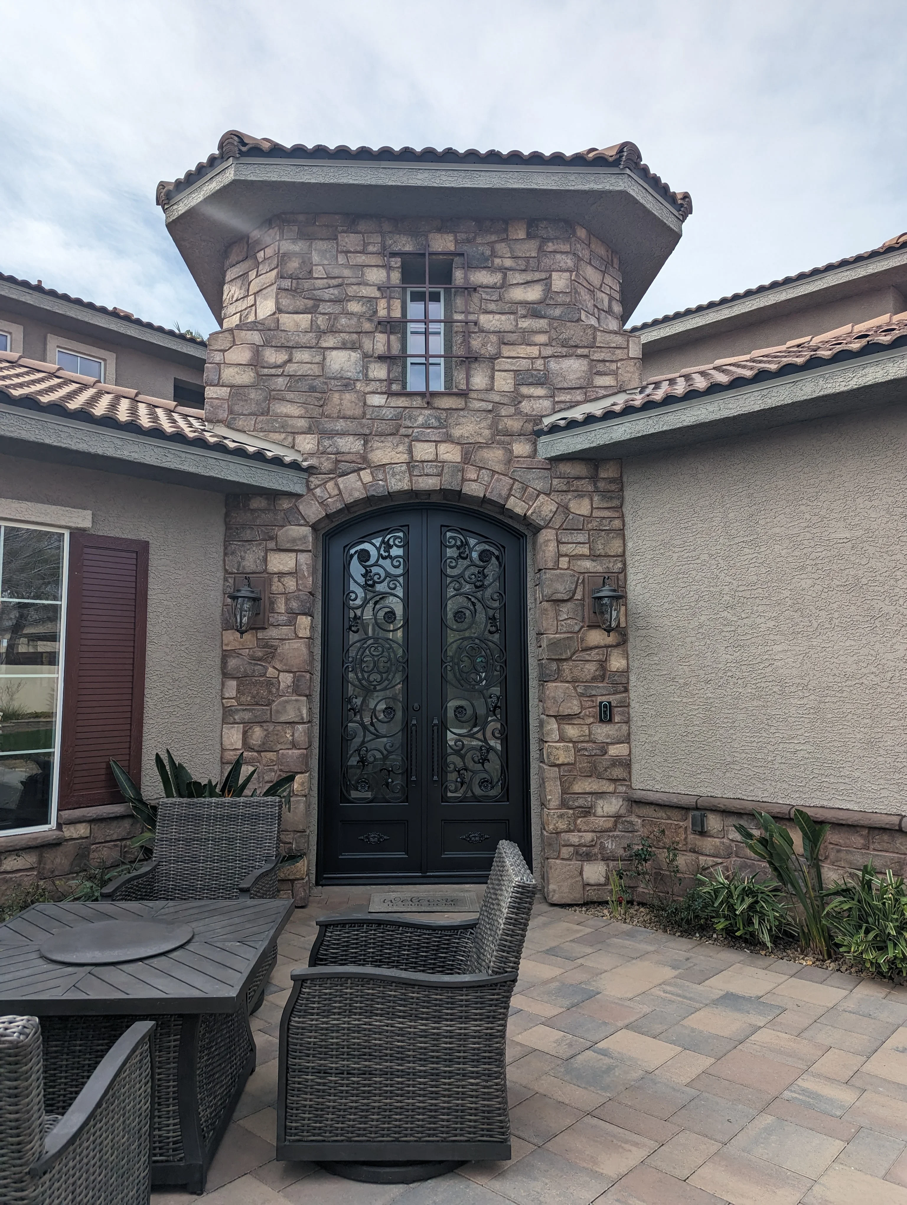Stone entry tower with black wrought iron doors and clay brick patio hardscape
