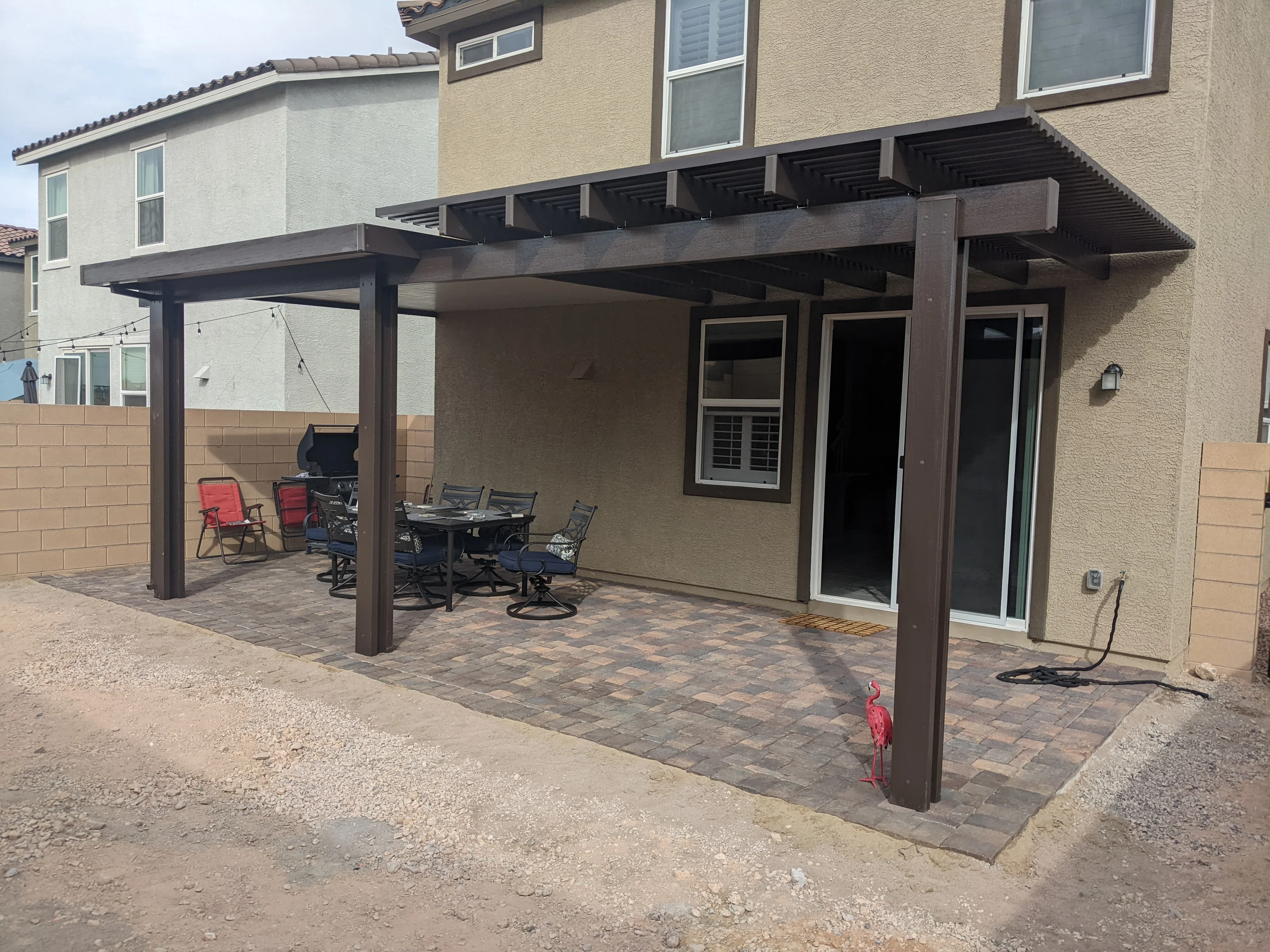 Dark steel pergola patio with pavers, dining furniture, and shade structure attached to home