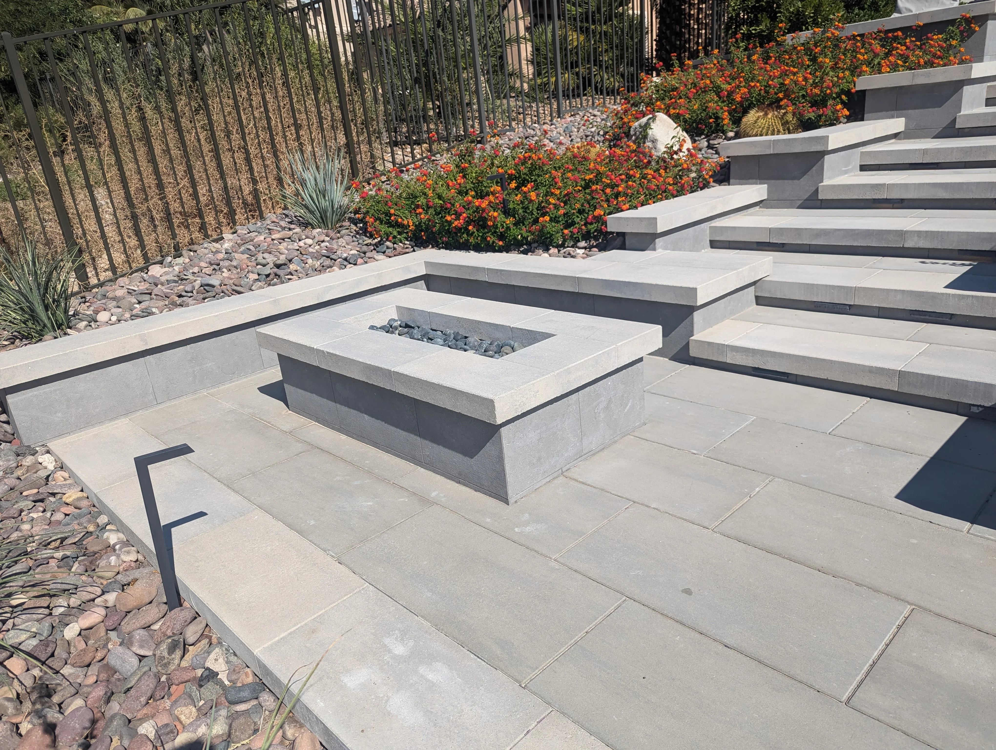 Modern concrete patio with central fire pit, tiered seating steps, and ornamental landscaping