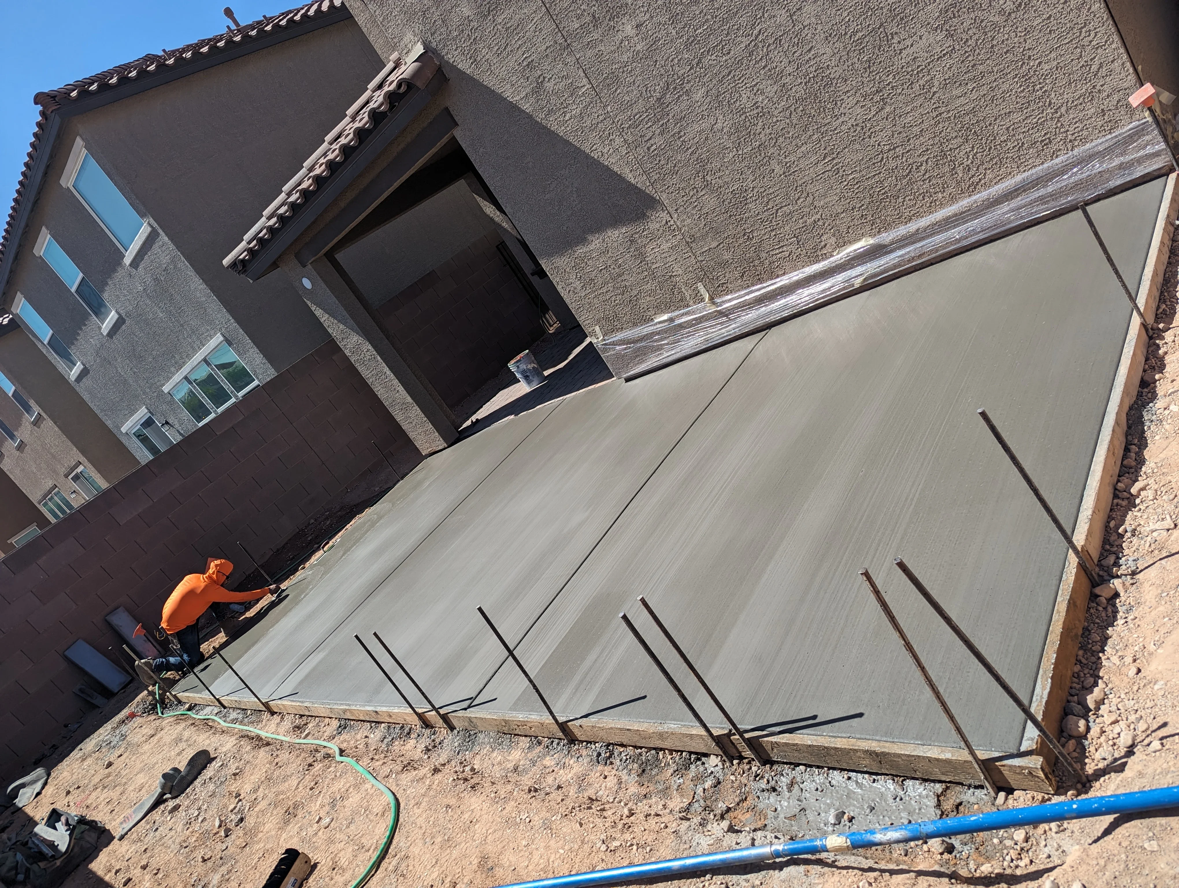 Concrete patio installation with rebar reinforcement and worker in orange shirt