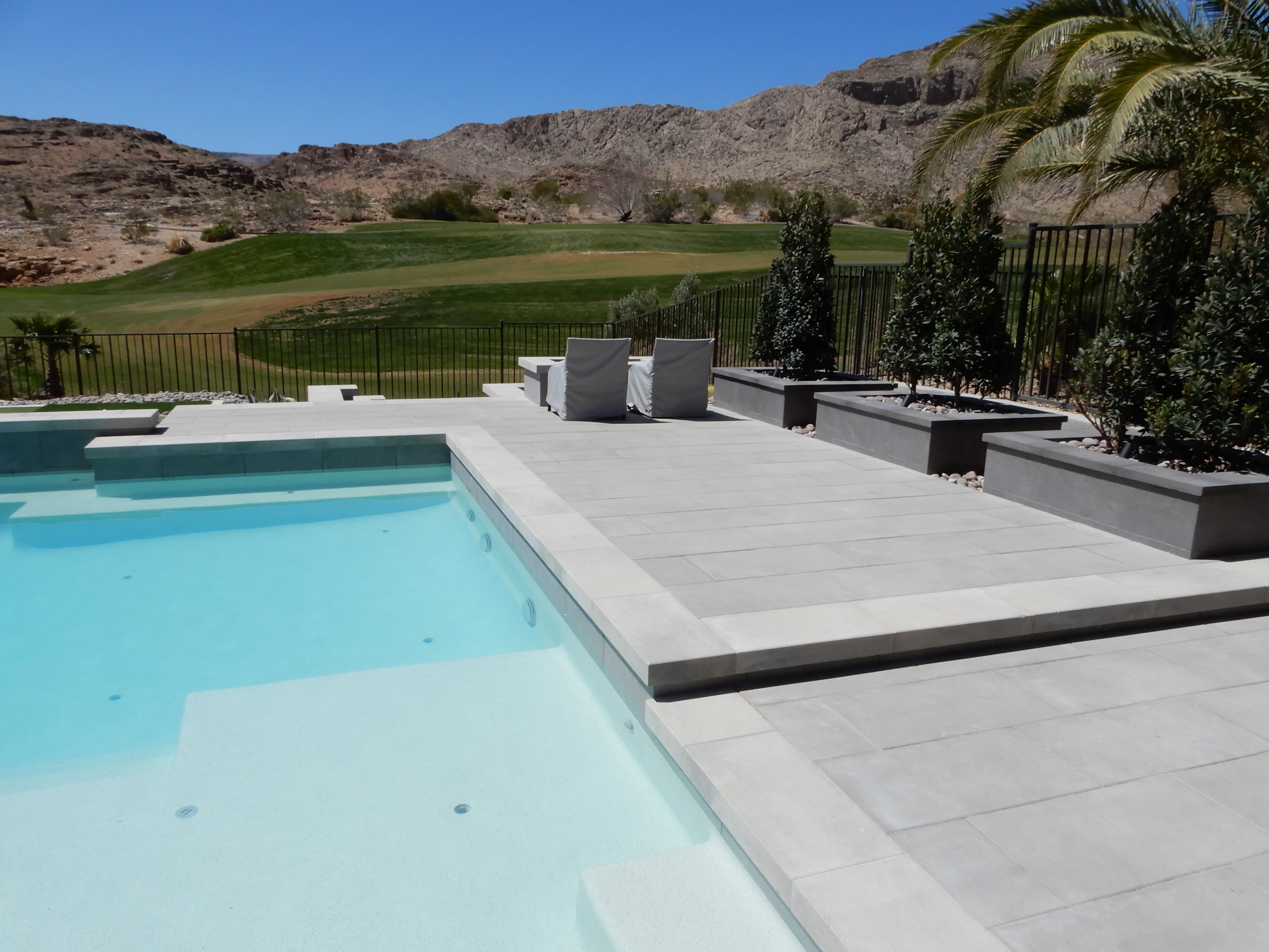 Modern poolside patio with gray pavers, lounge chairs, and golf course views