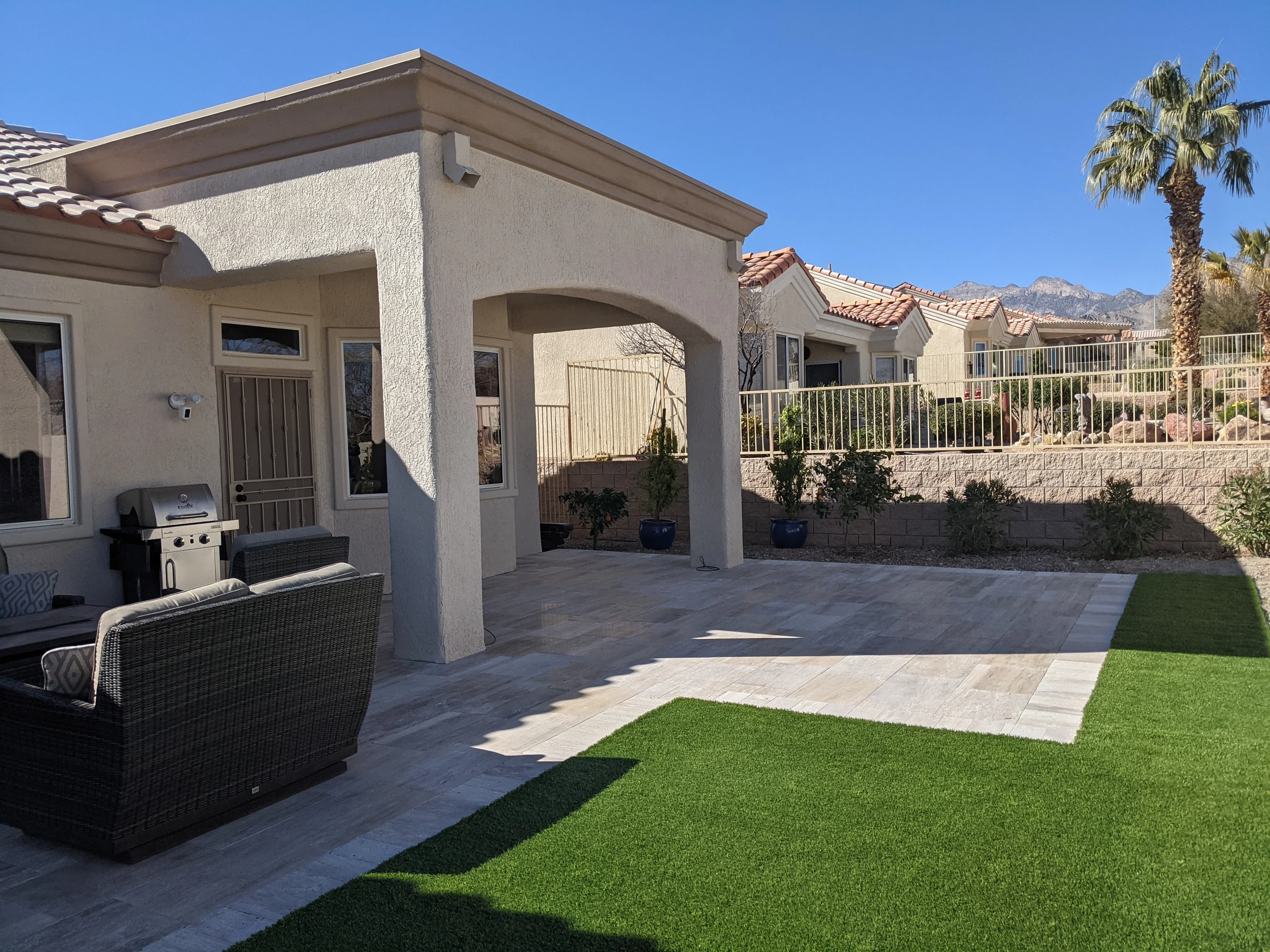 Modern patio with white pergola, pavers, synthetic grass, and stone retaining wall