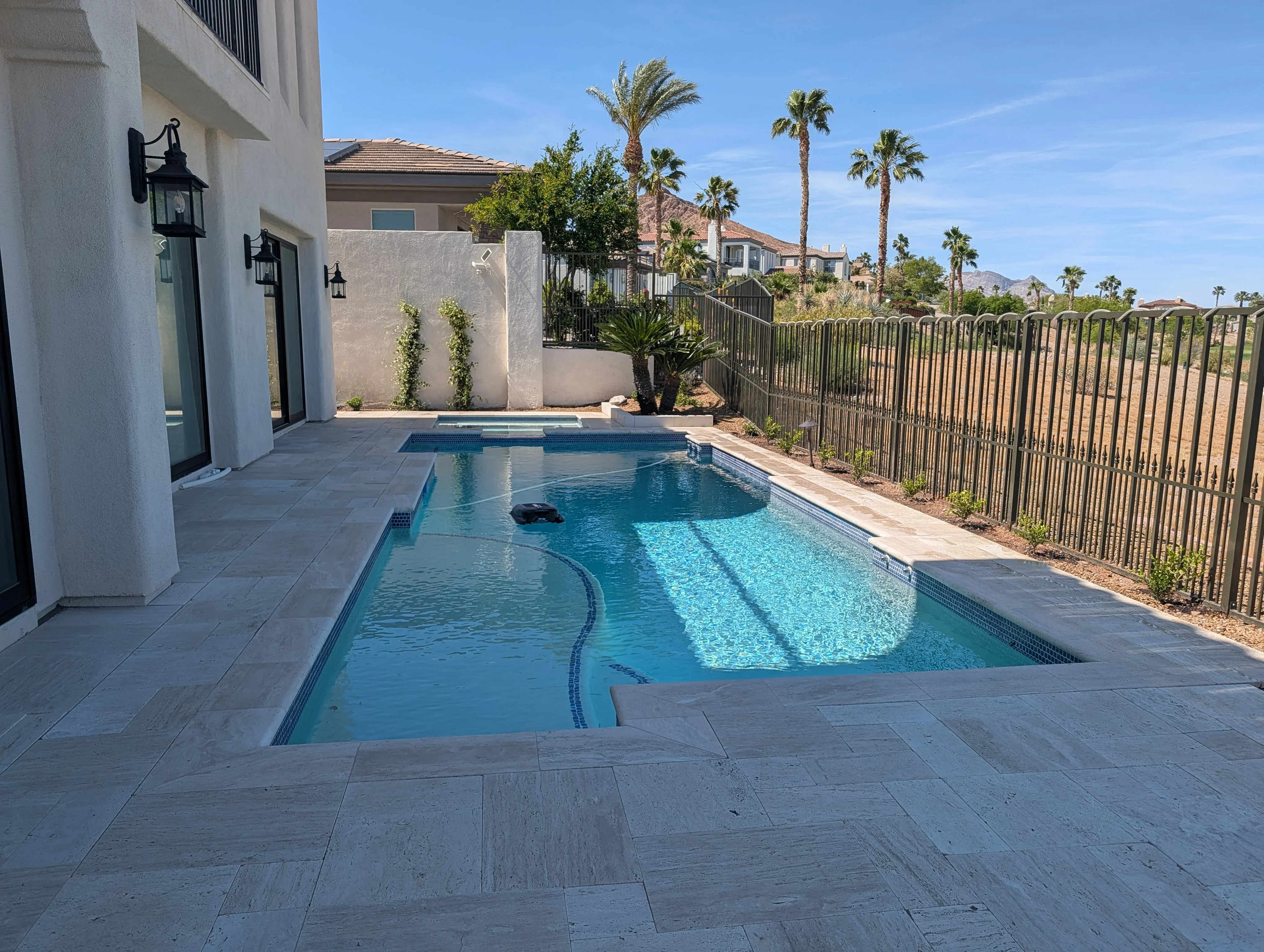 Modern backyard pool with travertine patio, privacy wall, and iron fencing in Las Vegas