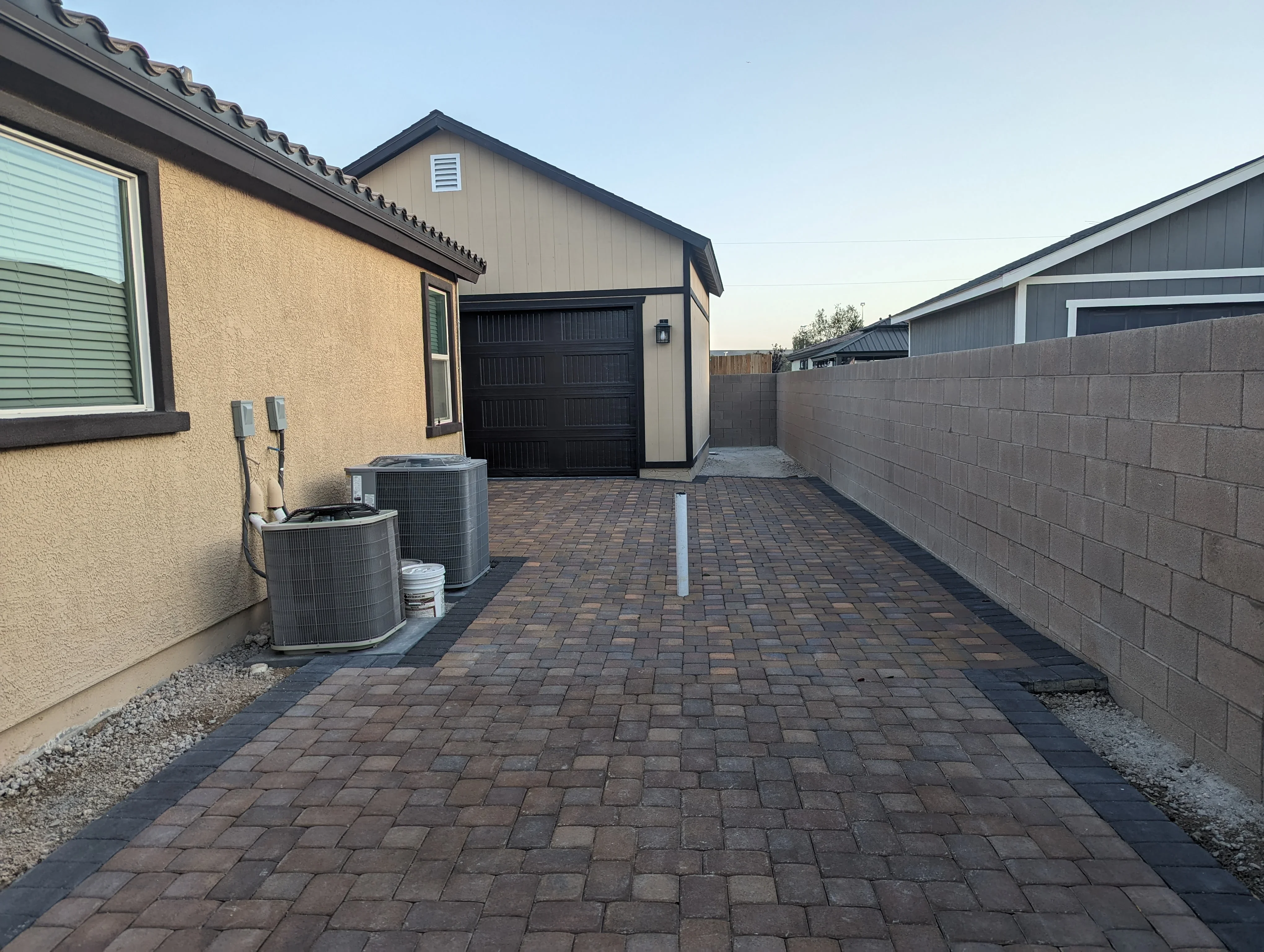 Newly installed brown and tan paver driveway with black garage door and block wall fencing