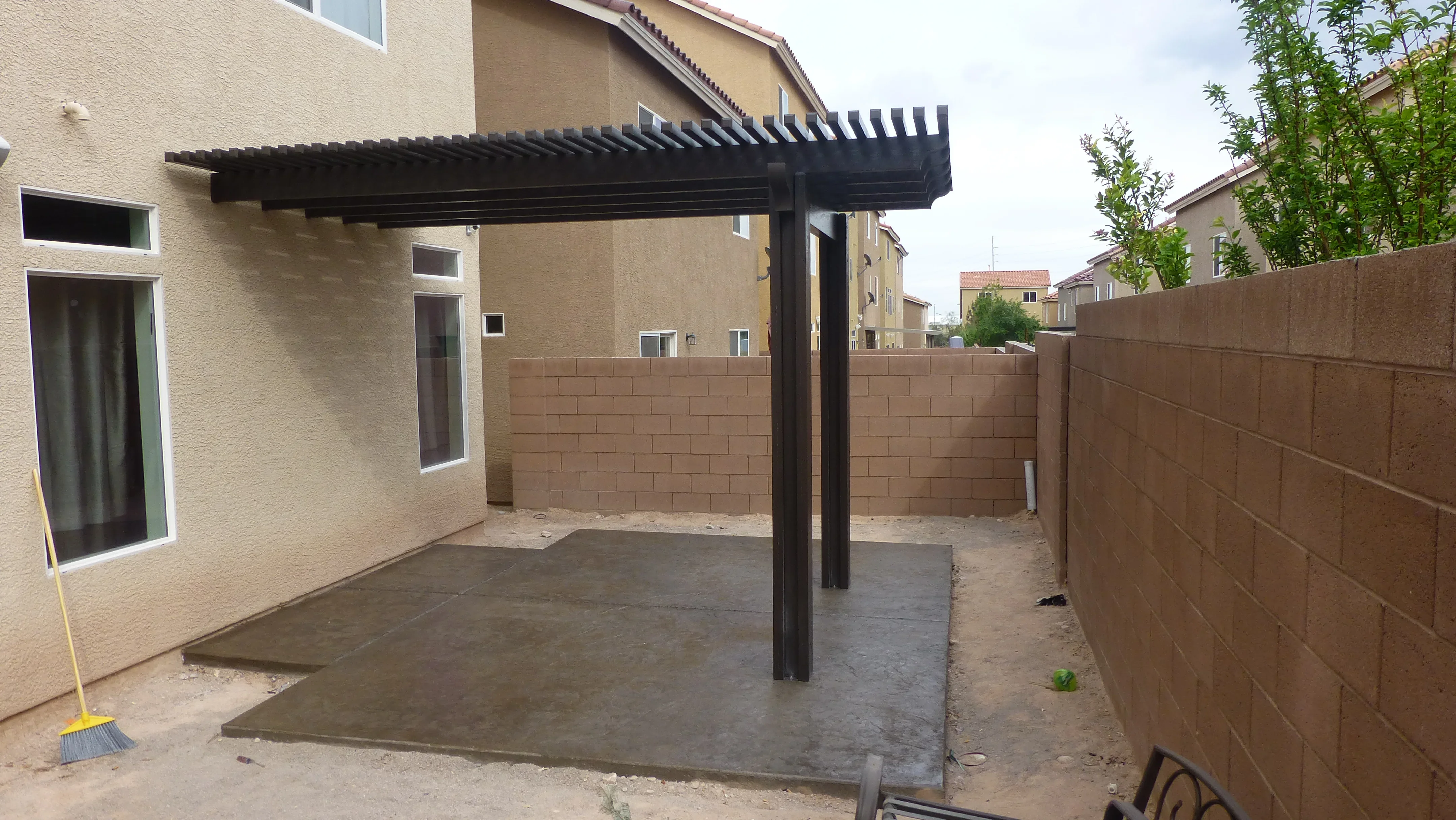 Black pergola over concrete patio with brown privacy fence in residential backyard