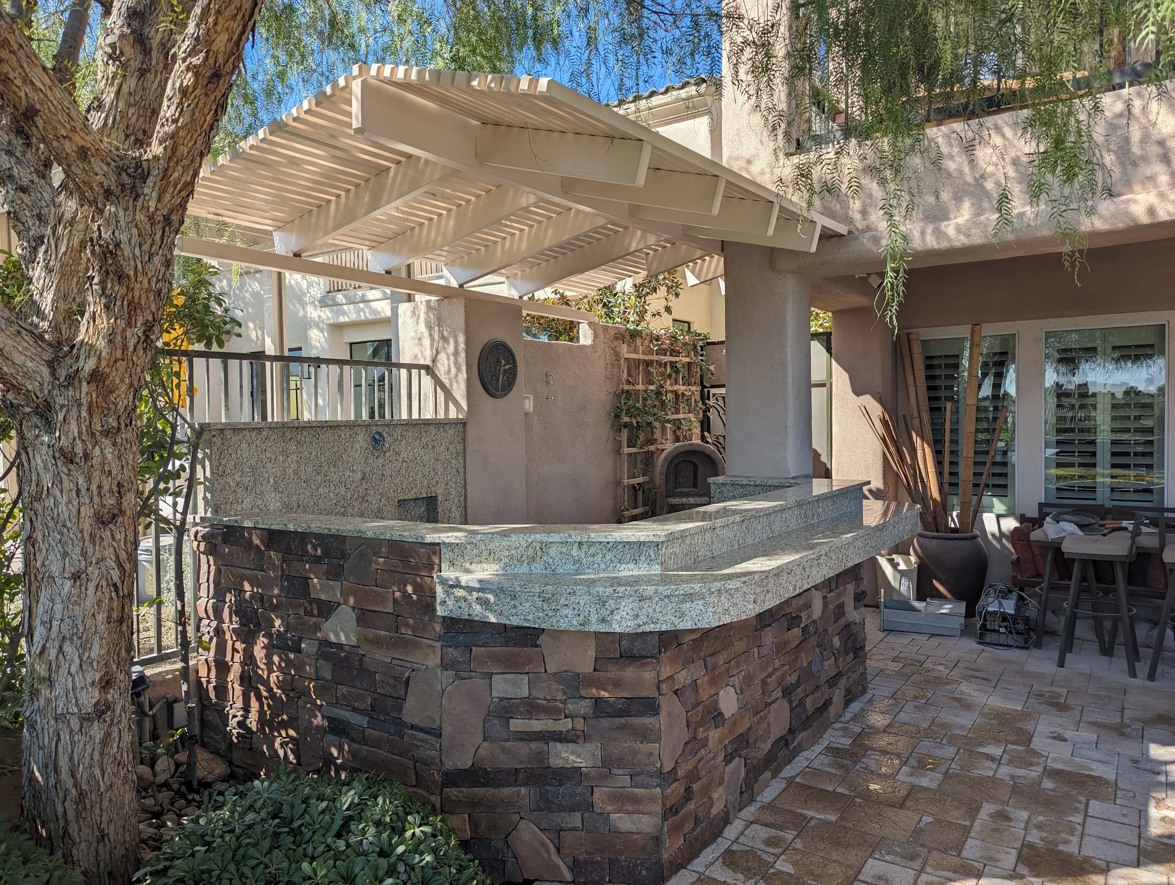 Curved stone bar with granite top and white pergola shade structure in backyard patio