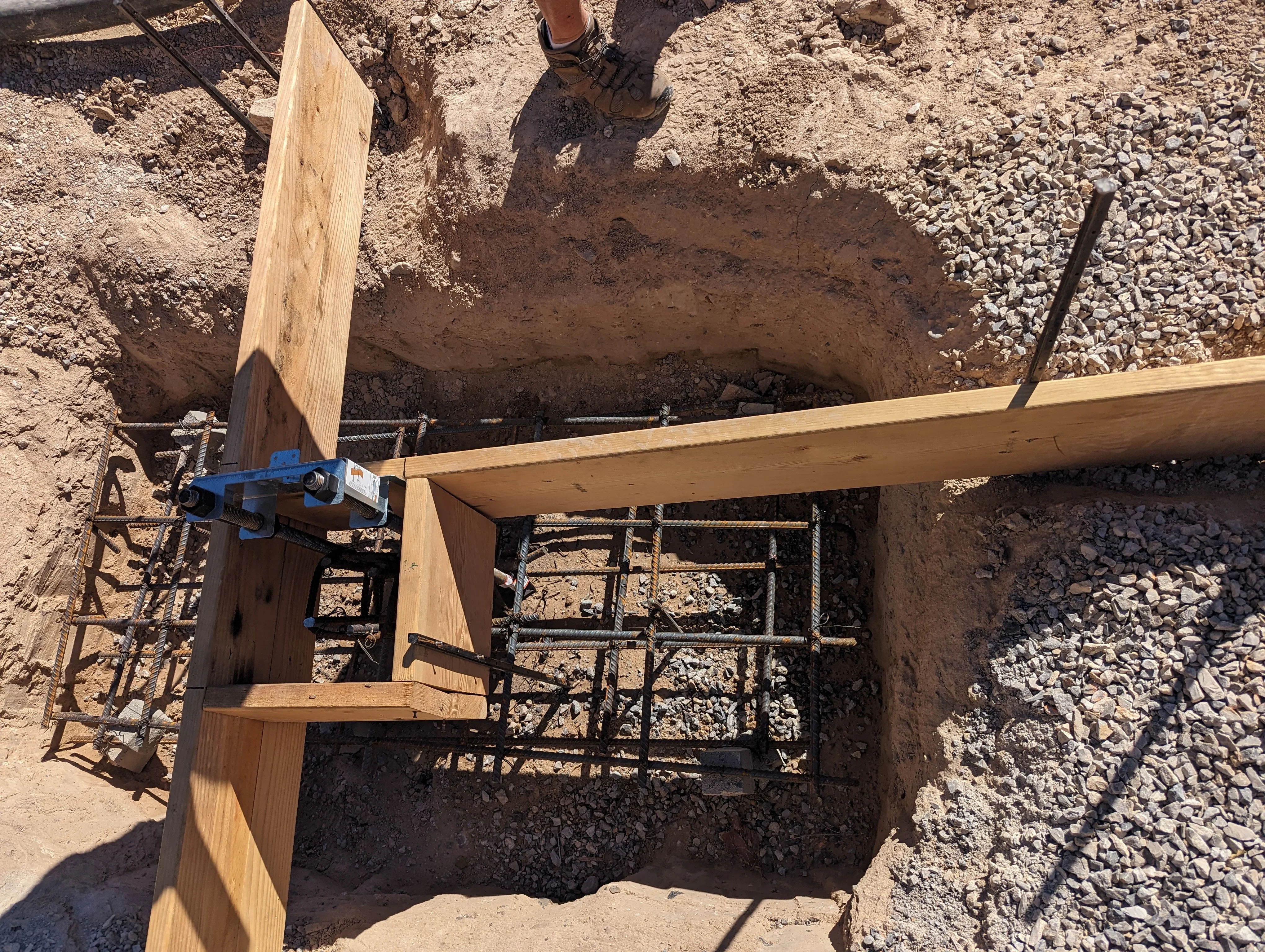 Wooden patio framing with blue brackets and rebar on excavated foundation site