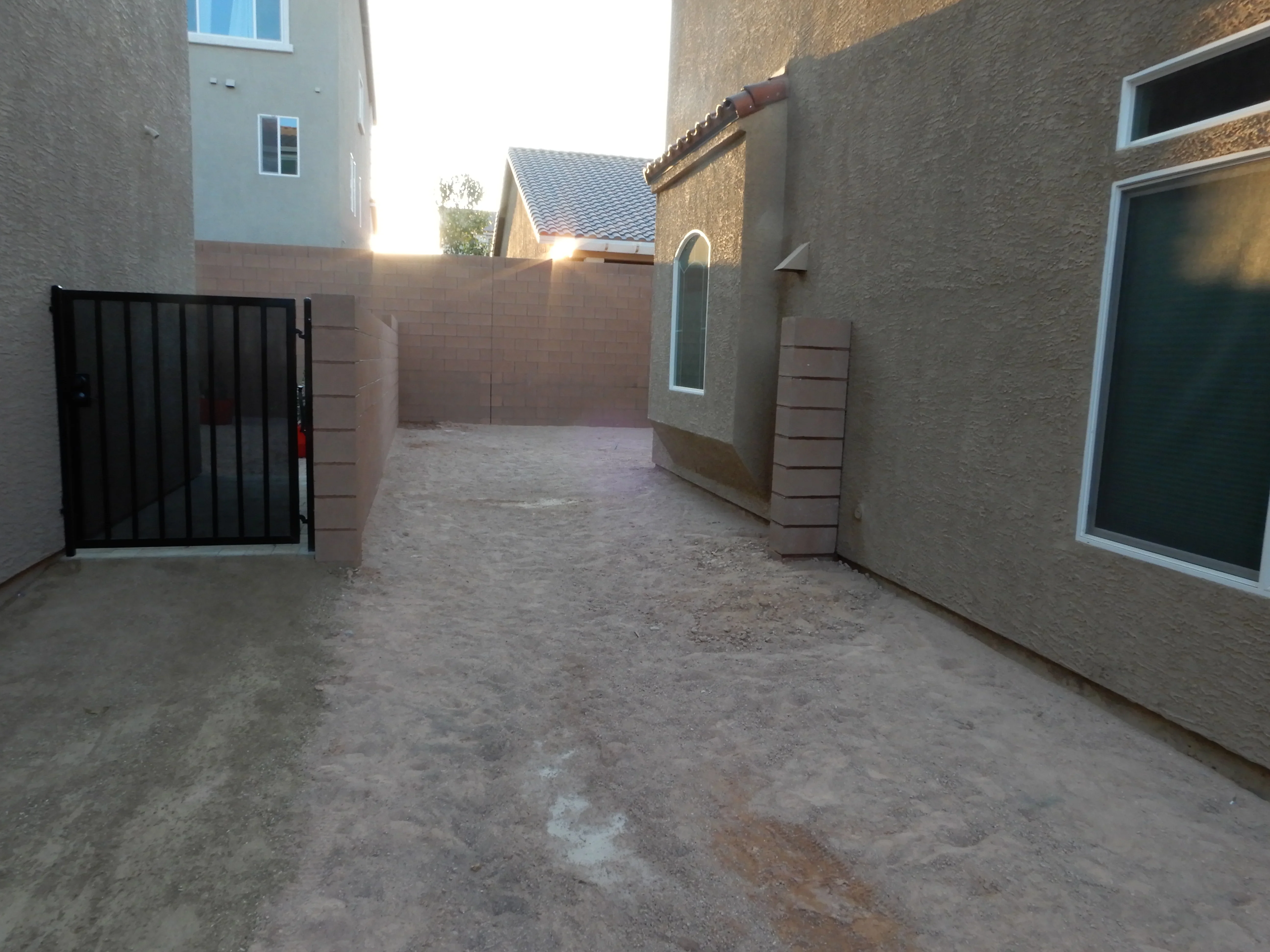 Concrete courtyard with stucco walls, black metal gate, and stone pilasters