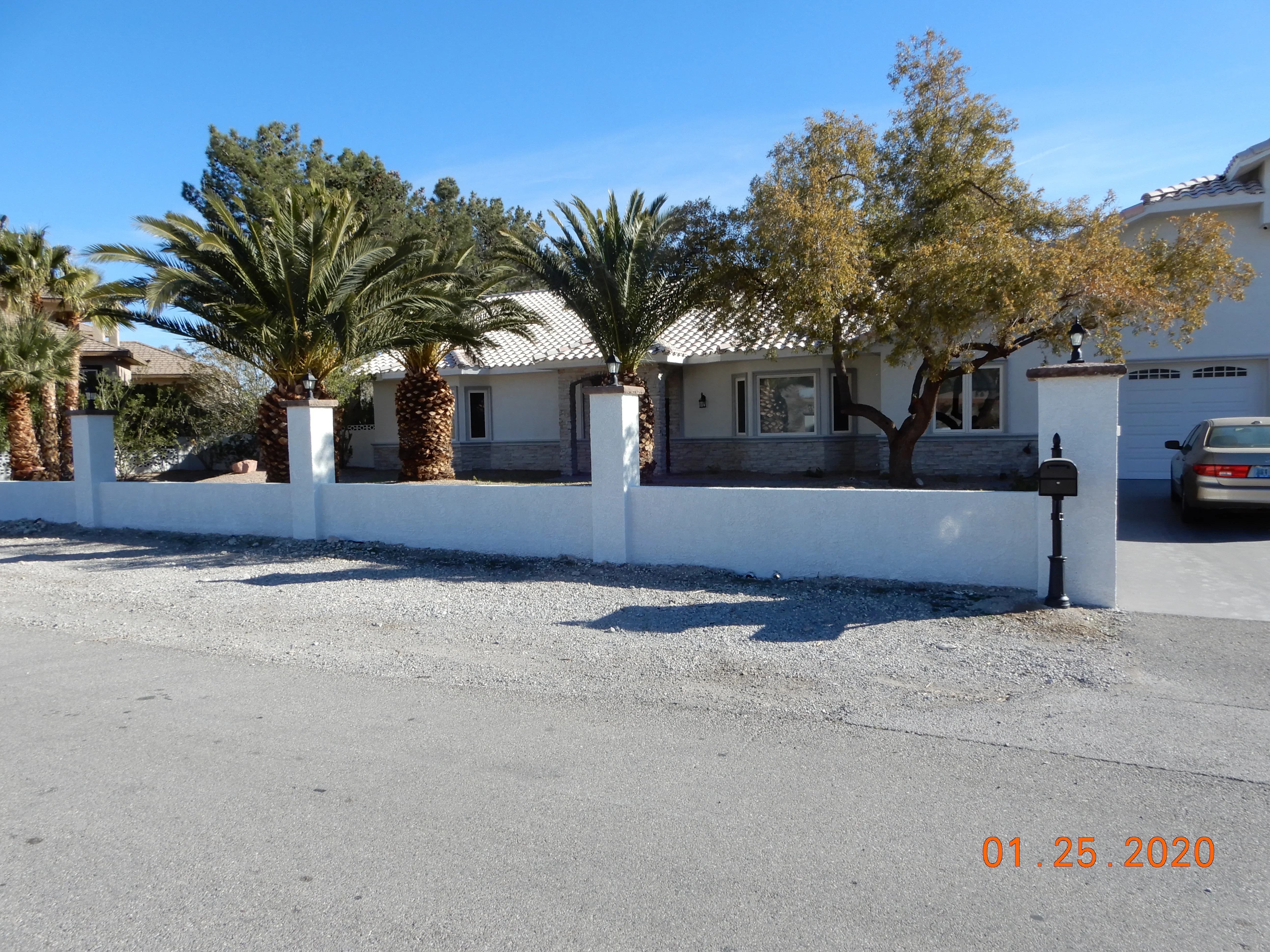 White stucco perimeter wall with stone base and palm tree landscaping on residential property